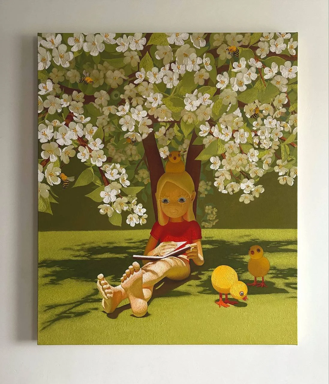 Painting by Nina Sechcko of a girl  under a blossoming apple tree, reading a book, with two yellow chick figurines nearby exhibited during art russia art fair by Robineau art 