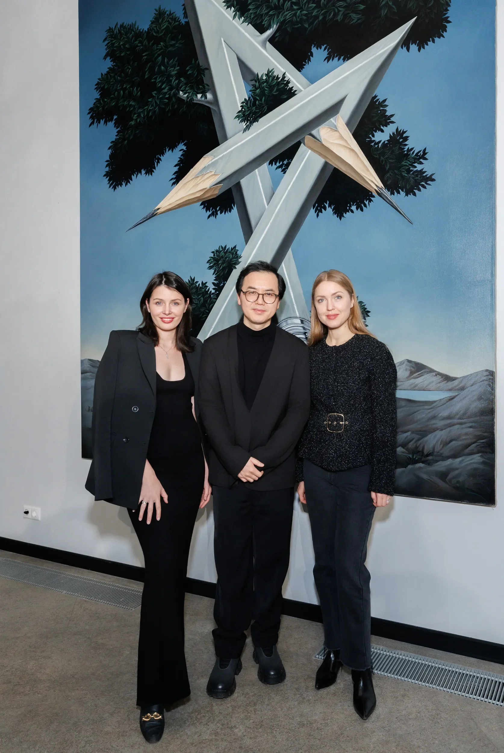 Three people posing in front of a large painting featuring abstract trees and mountains.