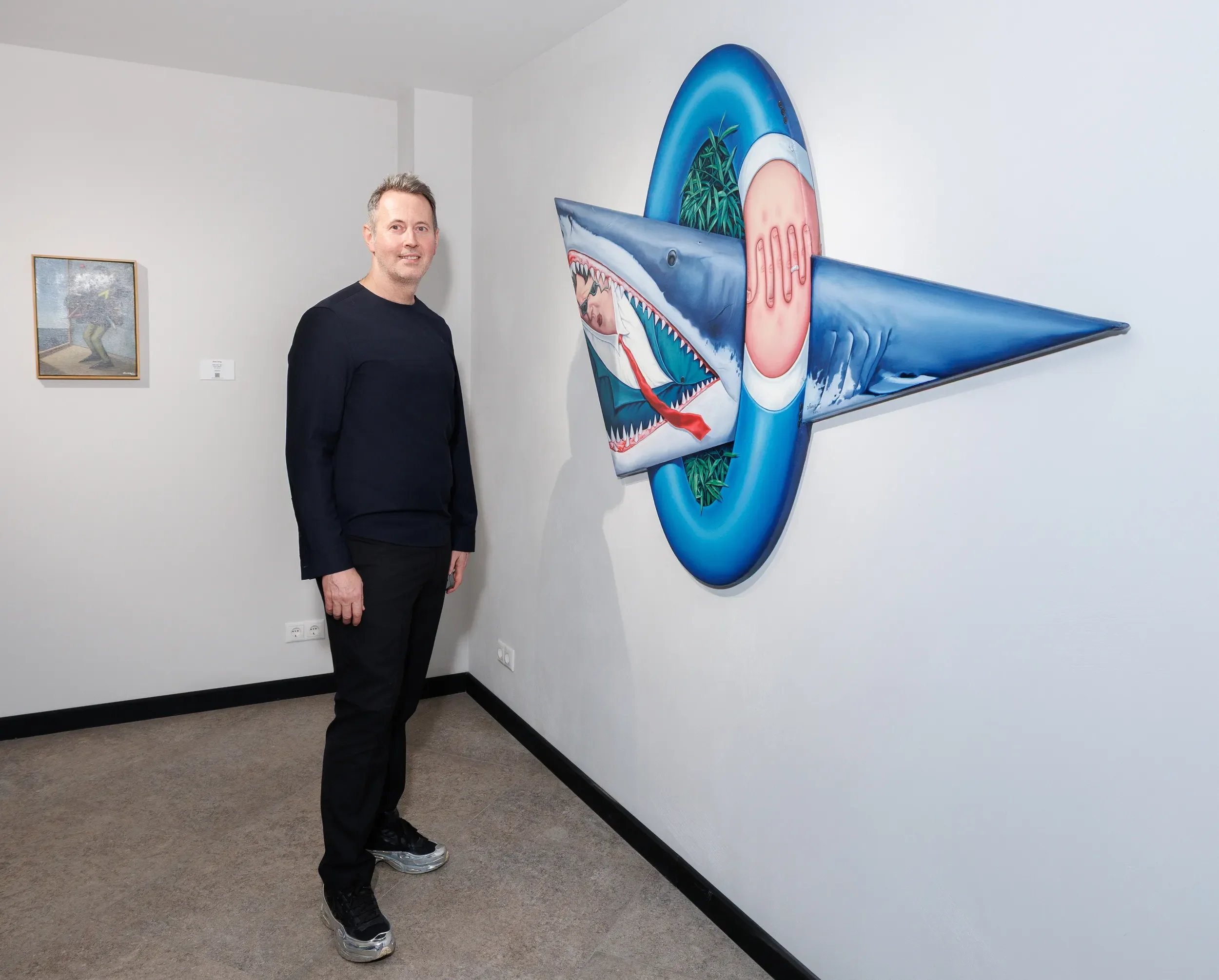A man standing next to a colorful, innovative airplane-shaped painting in an art gallery.