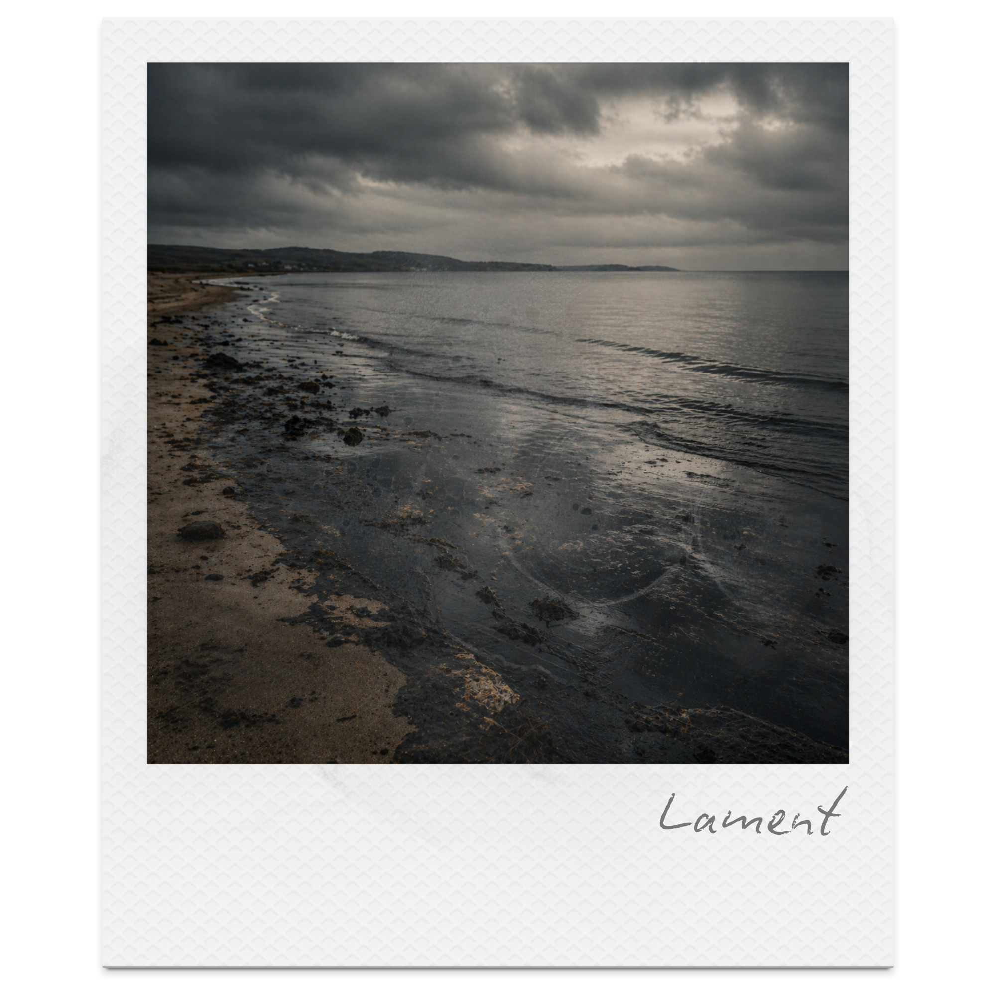 Photo of a beach with dark clouds overhead, calm water, and a distant shoreline.