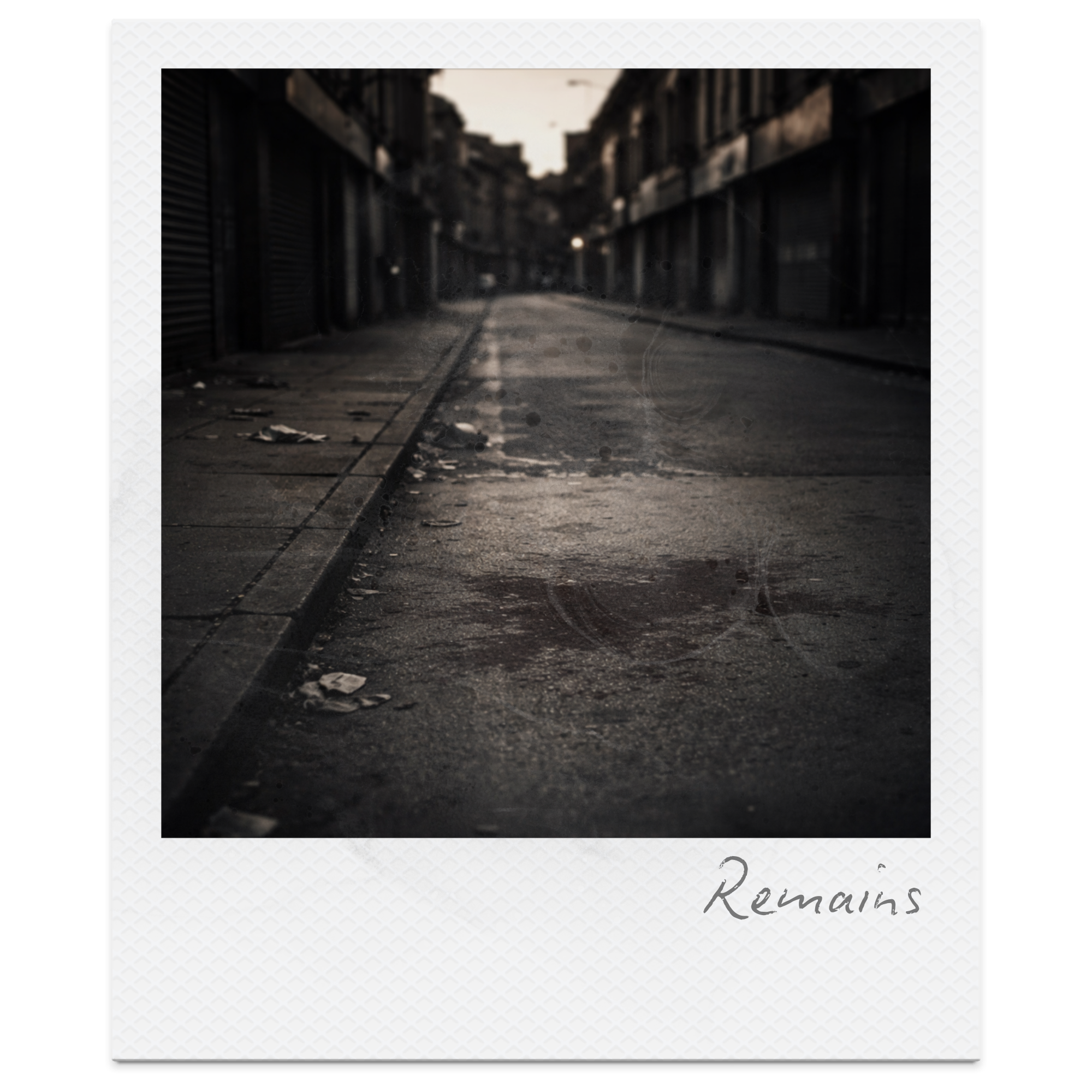 Empty urban street at dusk with litter and wear on the pavement, buildings with storefronts on both sides, and a distant horizon. The word 'Remains' is handwritten on the bottom right of the image.