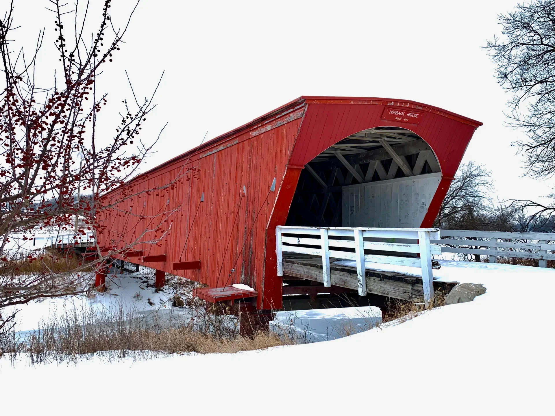 Red covered bridge with white fence over a creek in a white winter