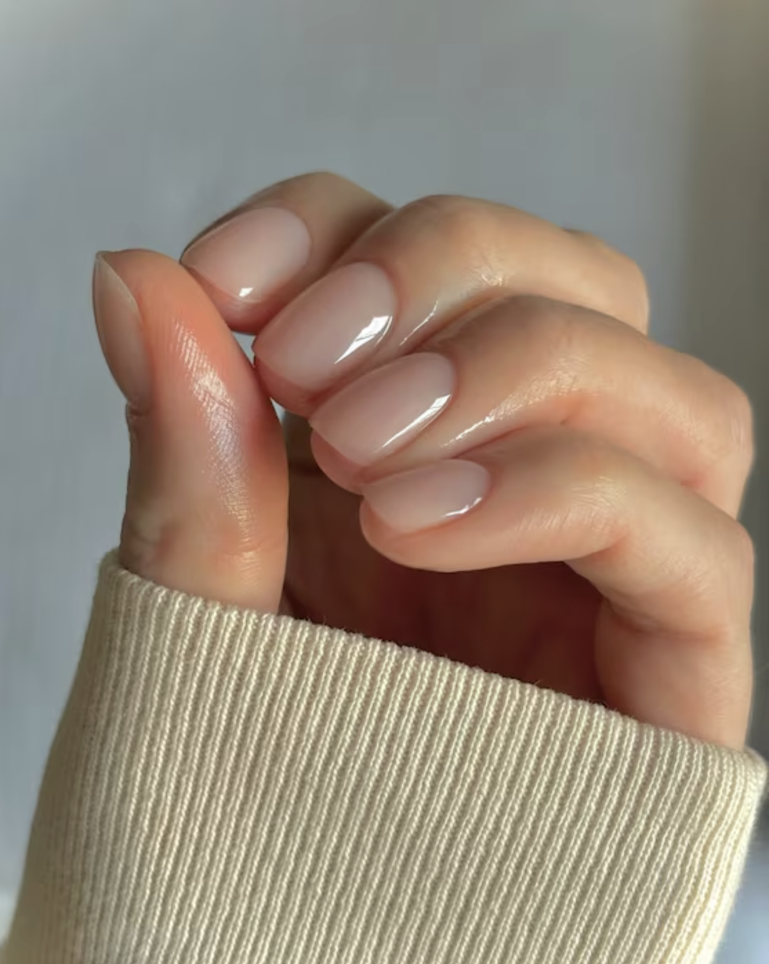 A hand with perfectly manicured, short, pink nails.  You can see the cuff of a knitted sleeve.