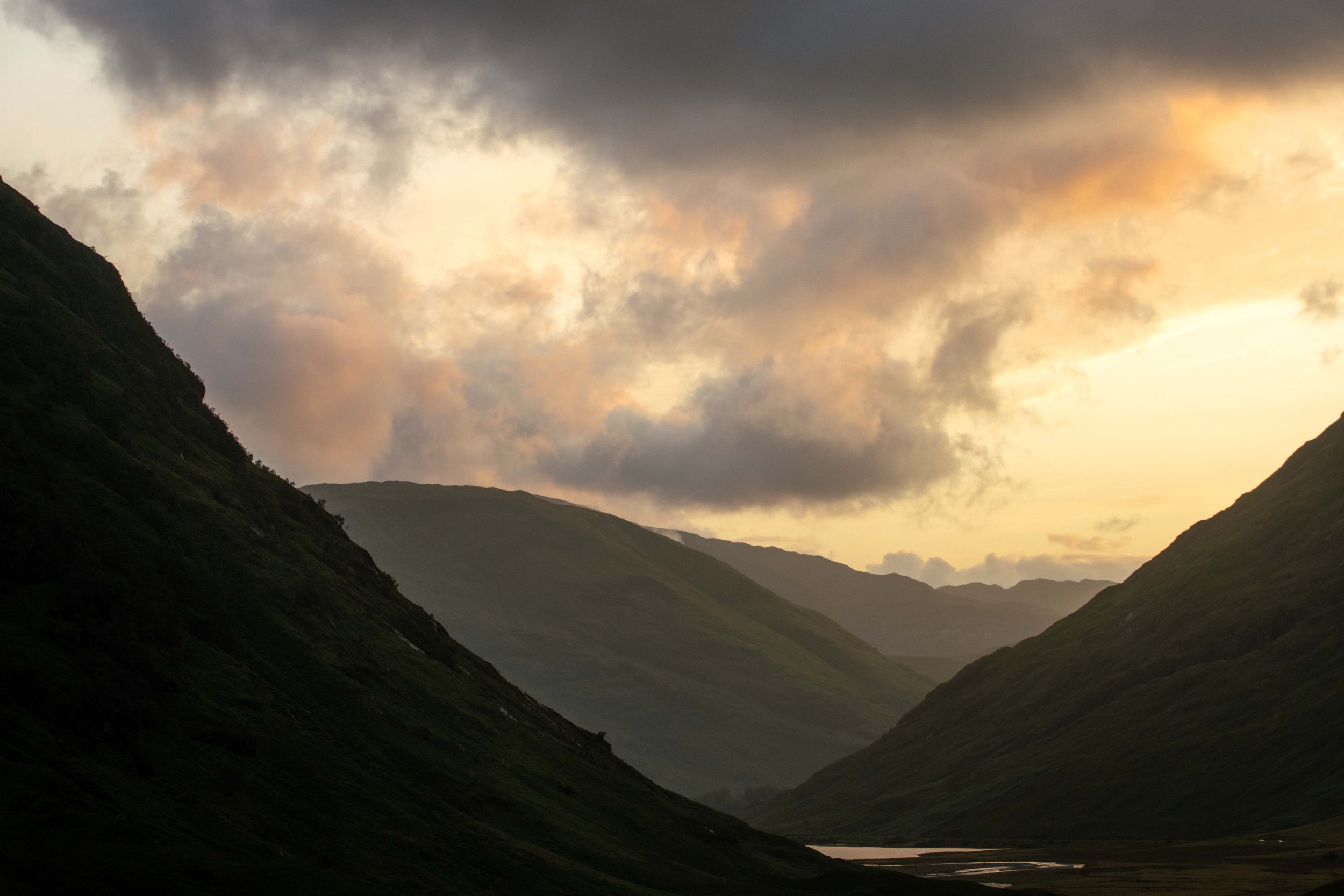 Scenic view of a mountain valley under cloudy sky at sunset