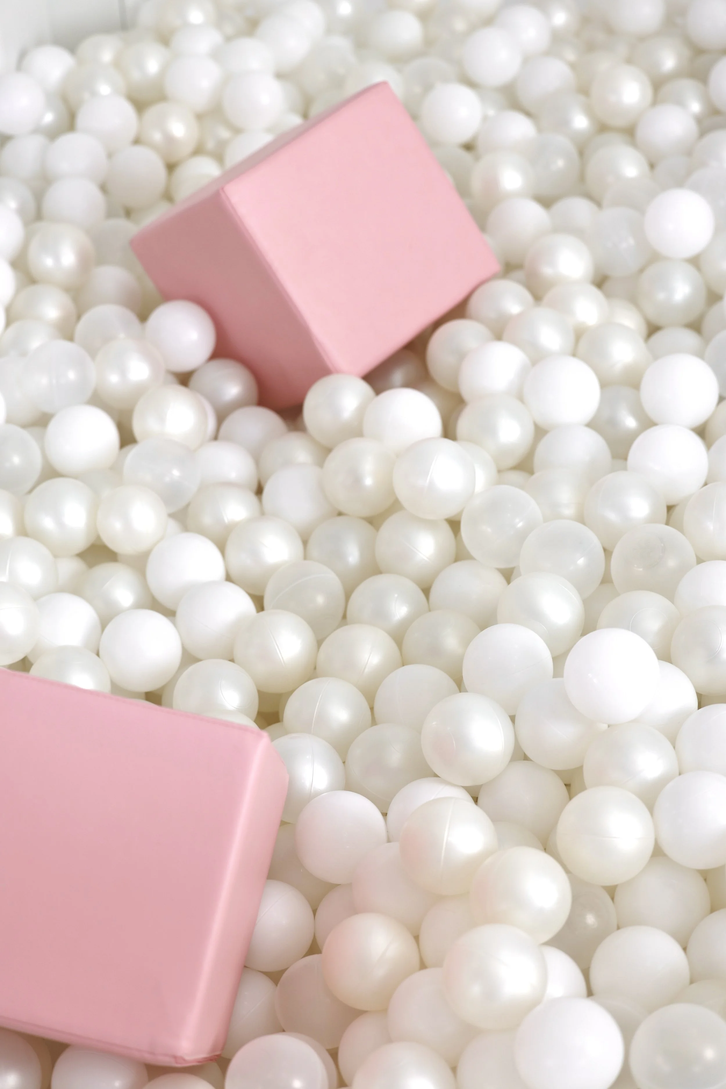 Pink block among white plastic balls in a ball pit.