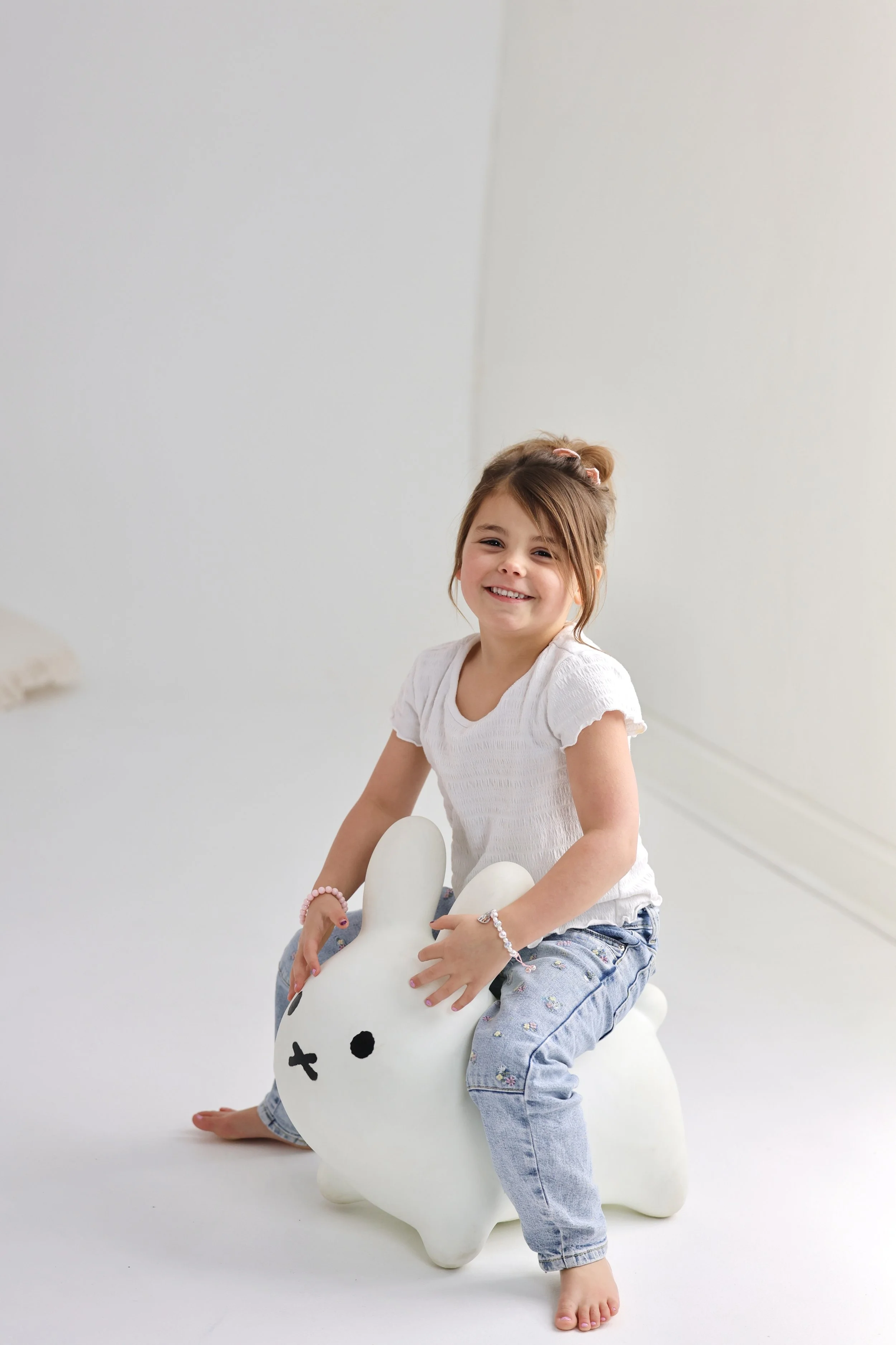 A young girl smiling while sitting on a white rabbit-shaped stool.