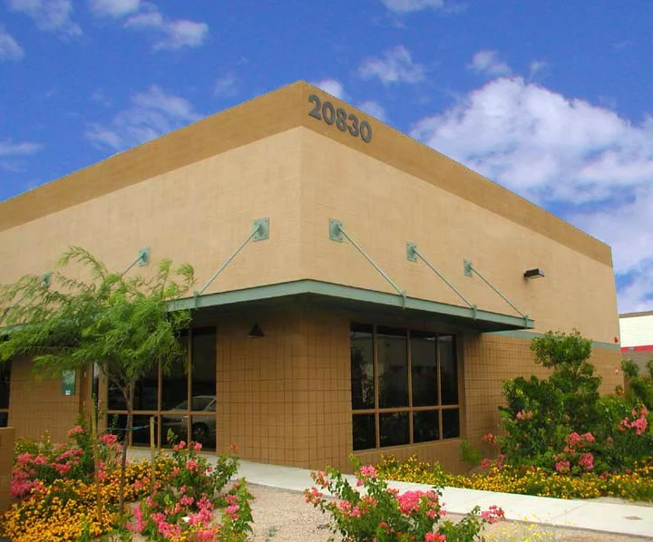 Modern commercial office building with beige CMU walls and large windows, surrounded by colorful landscaping.