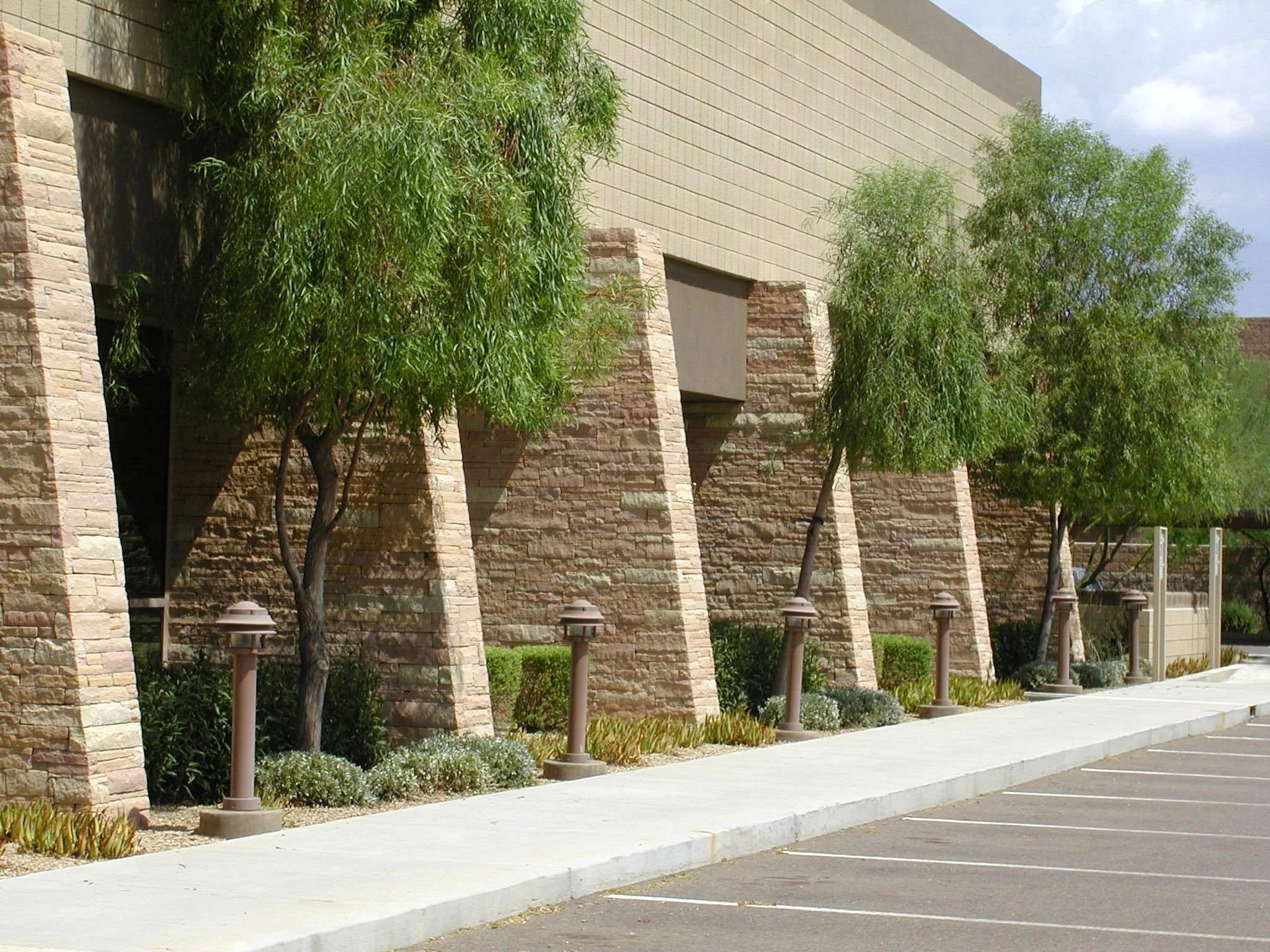 Modern industrial building exterior with stone walls, trees, and outdoor lights in a parking lot.
