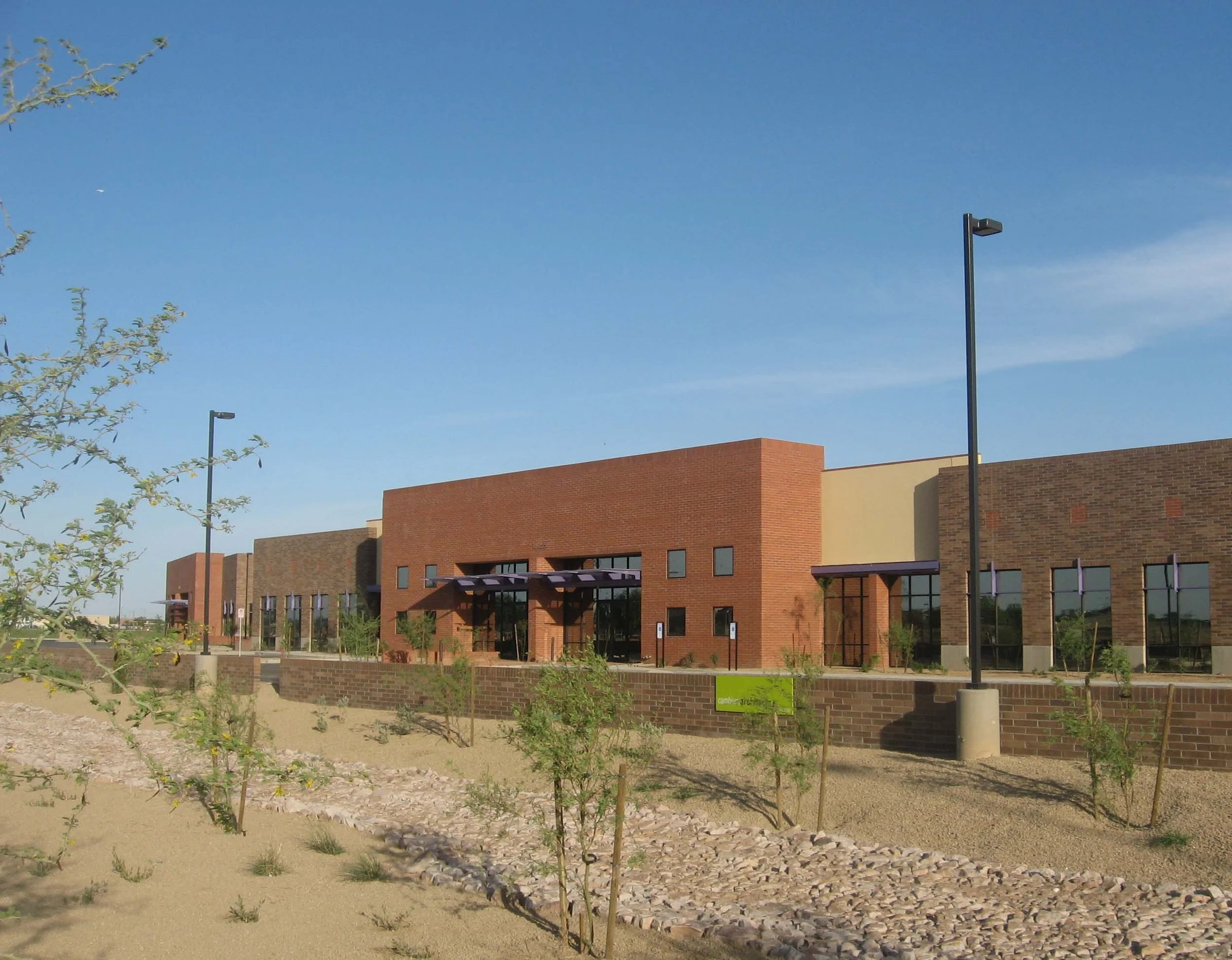 Exterior of a modern office building with brick façade and large windows, surrounded by desert landscaping and clear blue sky.