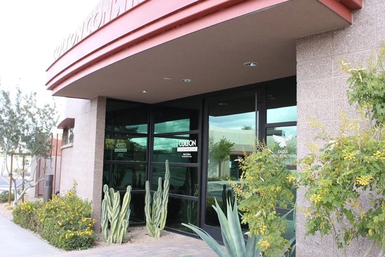 Entrance to a Colton Construction office building with glass doors and desert landscaping featuring cacti and shrubs.
