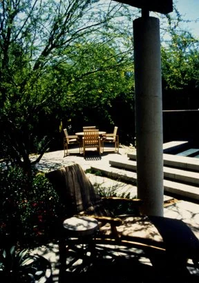 Outdoor patio with chairs, table, trees, and steps in sunlight