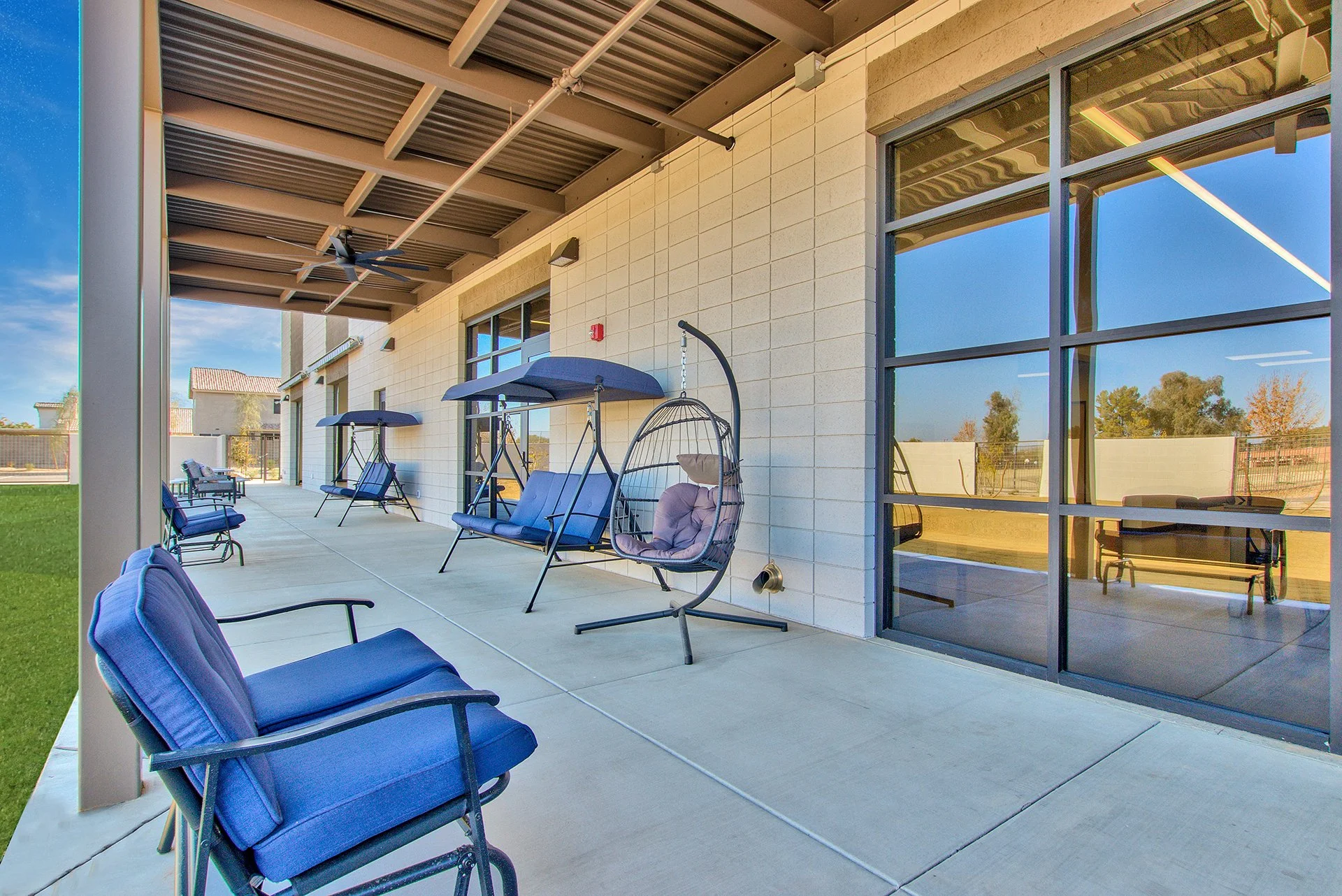 Outdoor patio with blue cushioned chairs, swinging benches with canopies, under a metal roof.