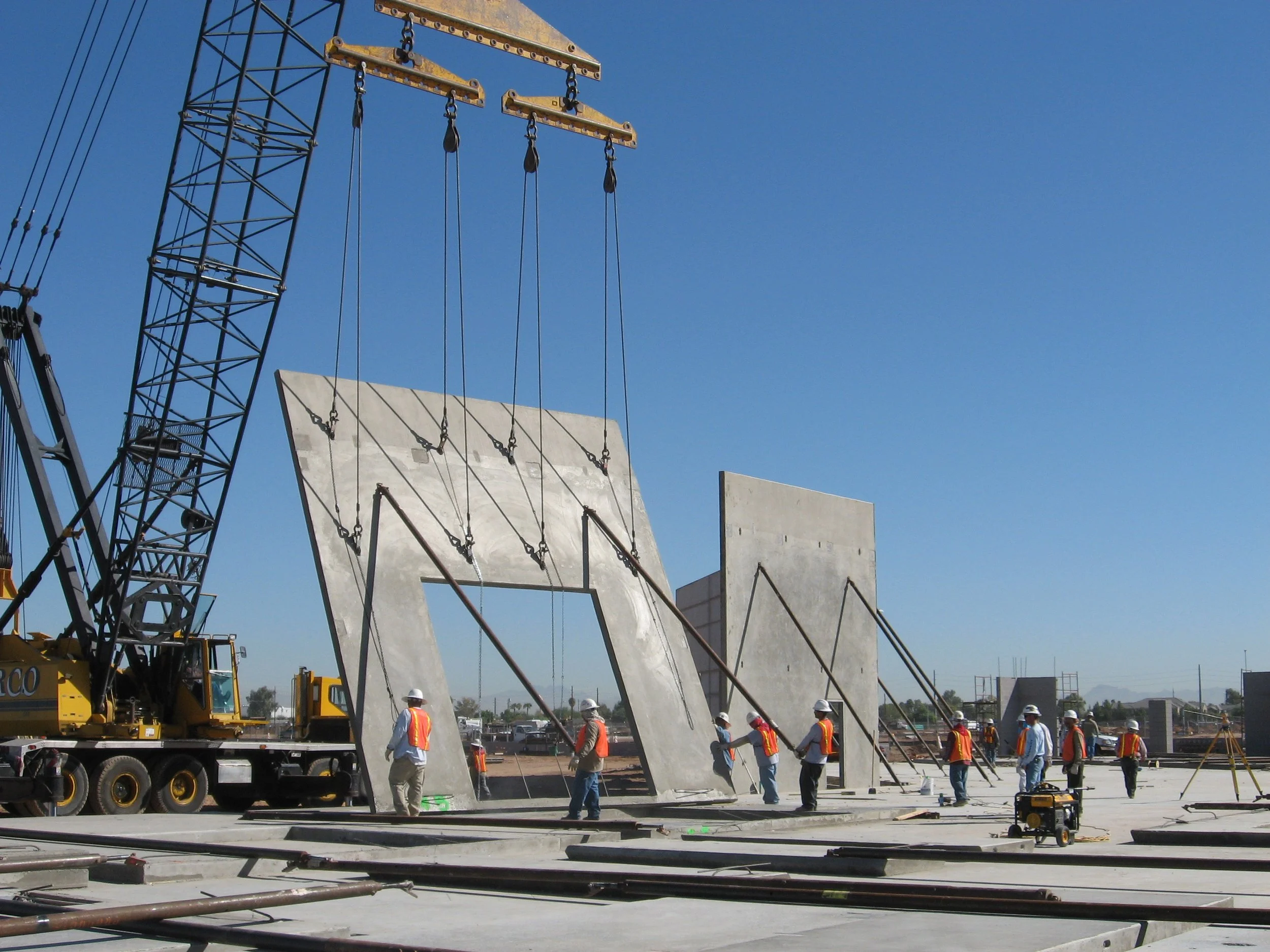 Construction site with crane lifting concrete wall panels and workers in safety vests and helmets.