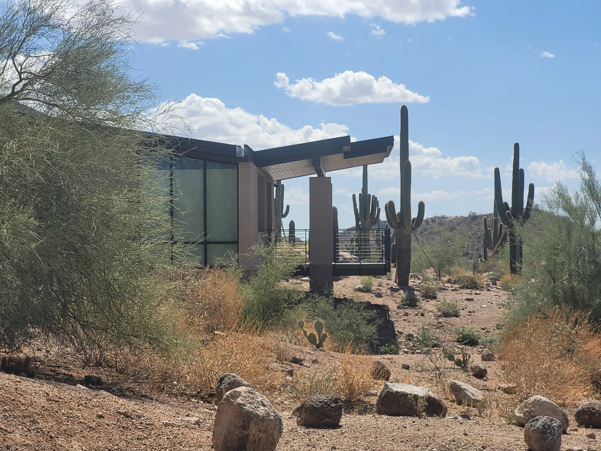 Desert landscape with modern casica, saguaro cacti, and rocky terrain under a clear blue sky.