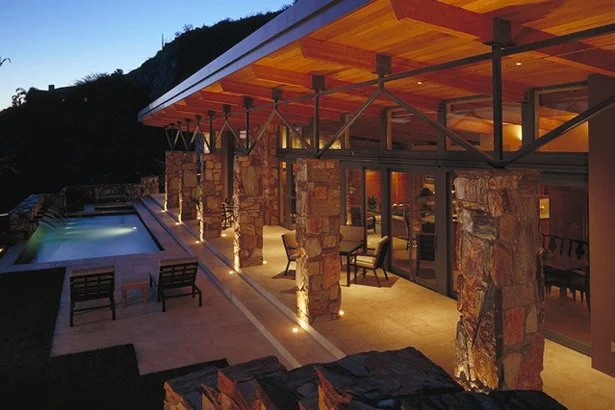 Contemporary house with illuminated stone pillars, glass walls, and a pool.