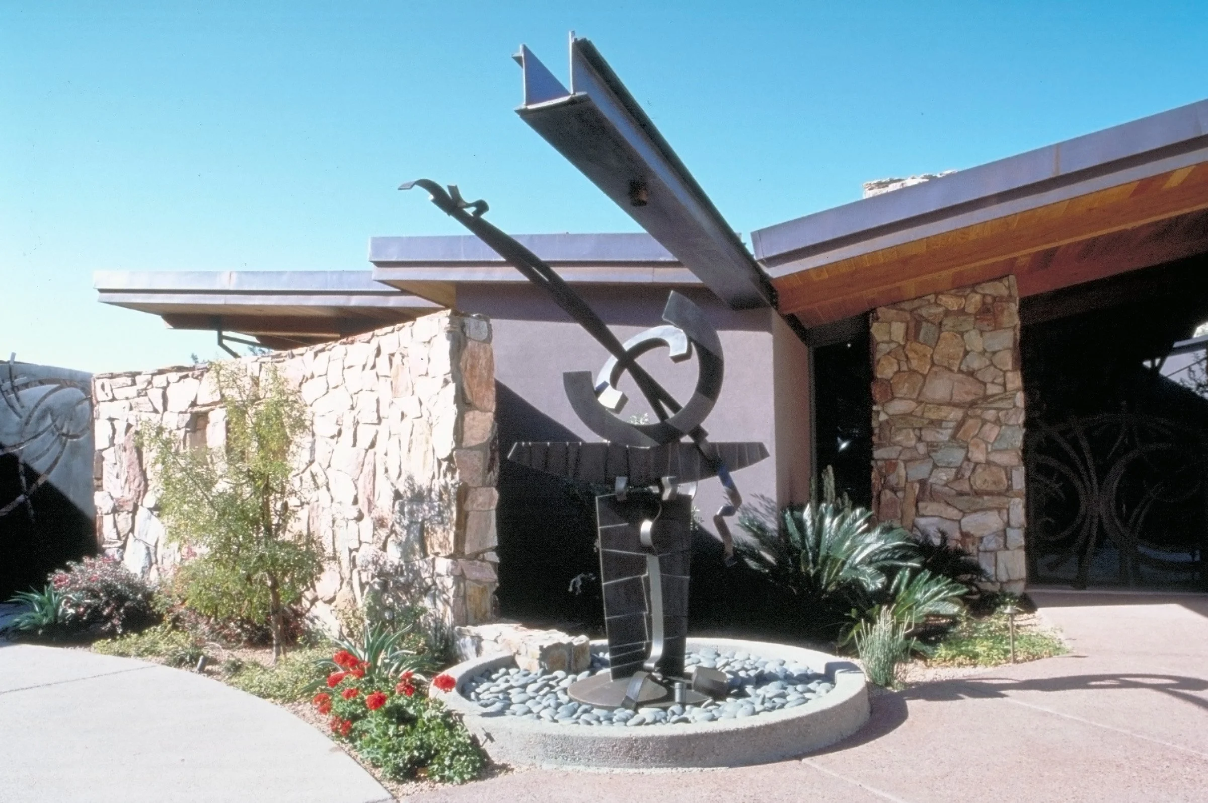 Modern metal sculpture outside a stone building with a garden