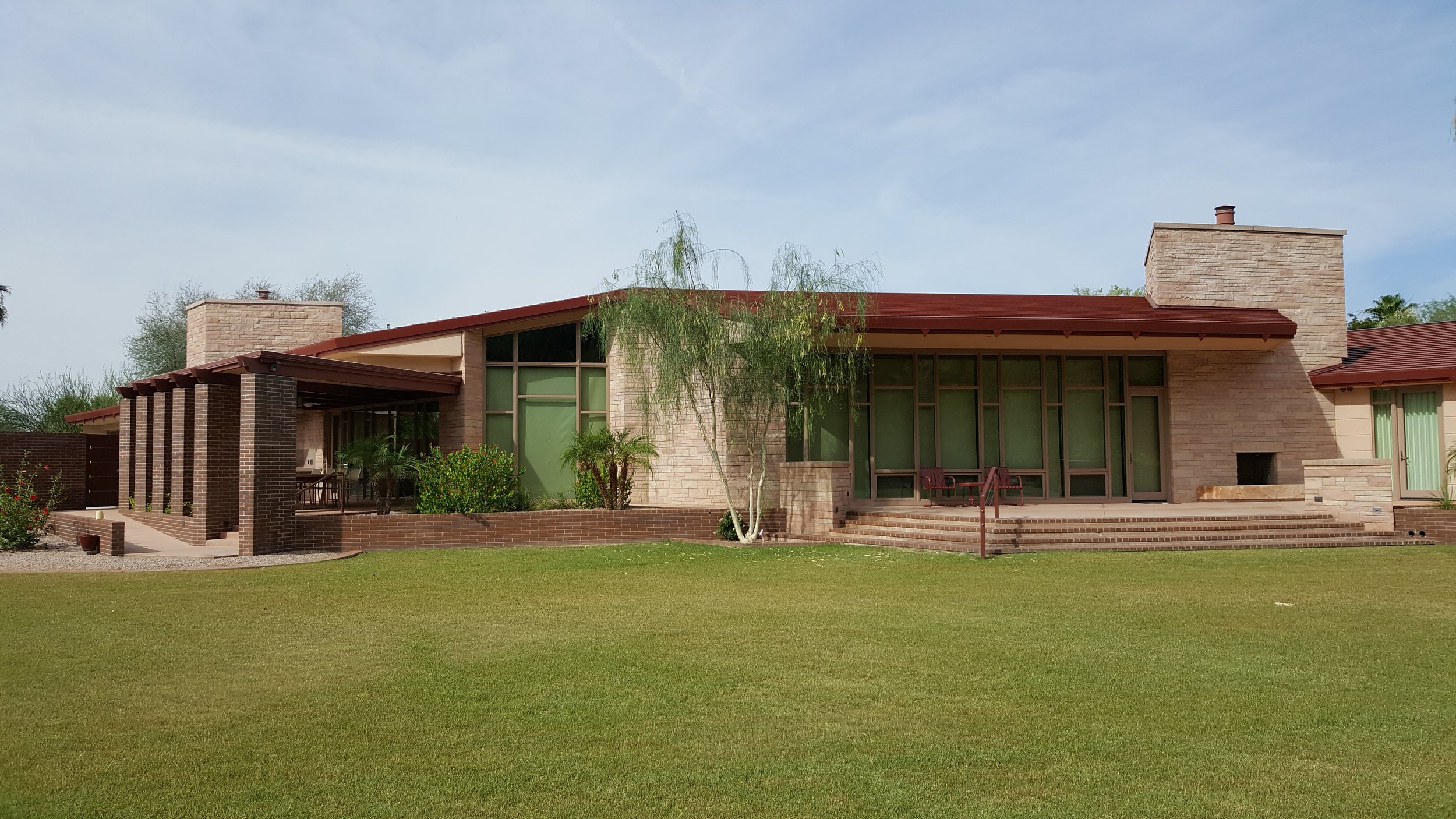 Single-story modern house with brick and stone exterior, large windows, a patio, and a lawn.
