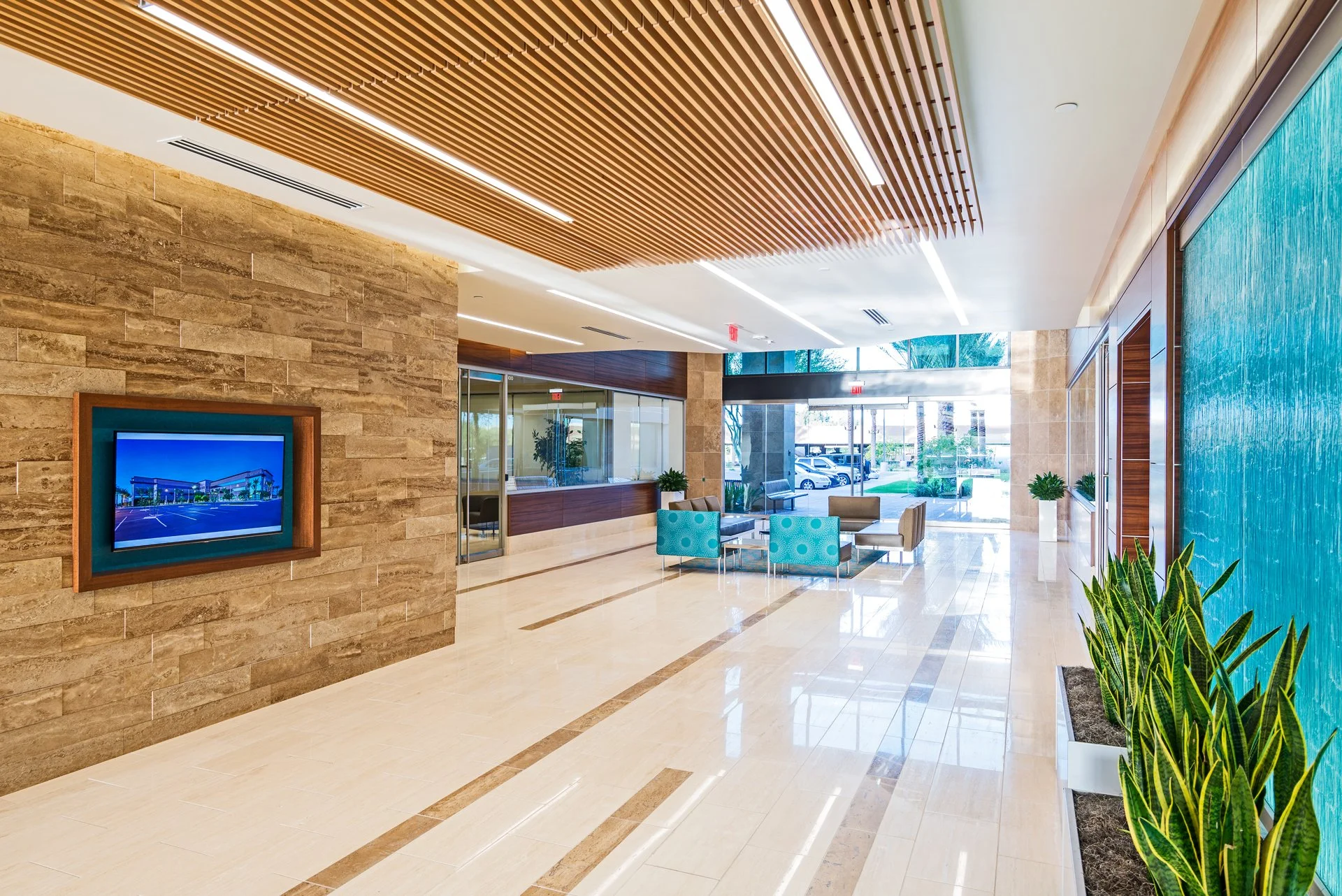 Modern office lobby with marble floors, wooden ceiling accents, a water feature wall, and seating area at Chandler 202.