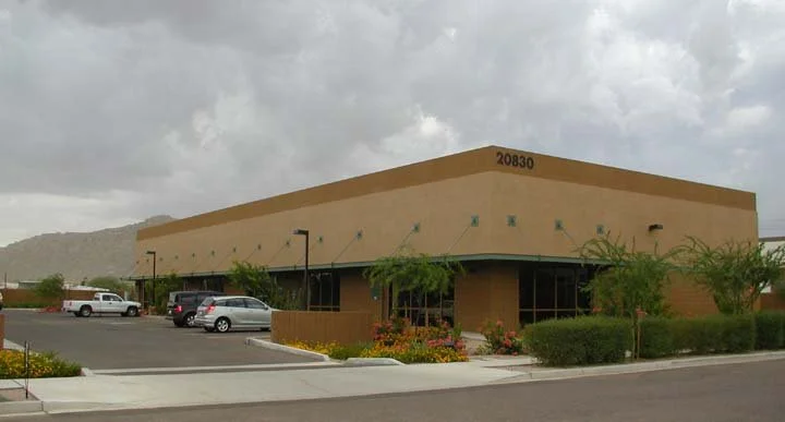 Single-story commercial office building with a flat roof and stucco exterior, surrounded by a parking lot and landscaping.