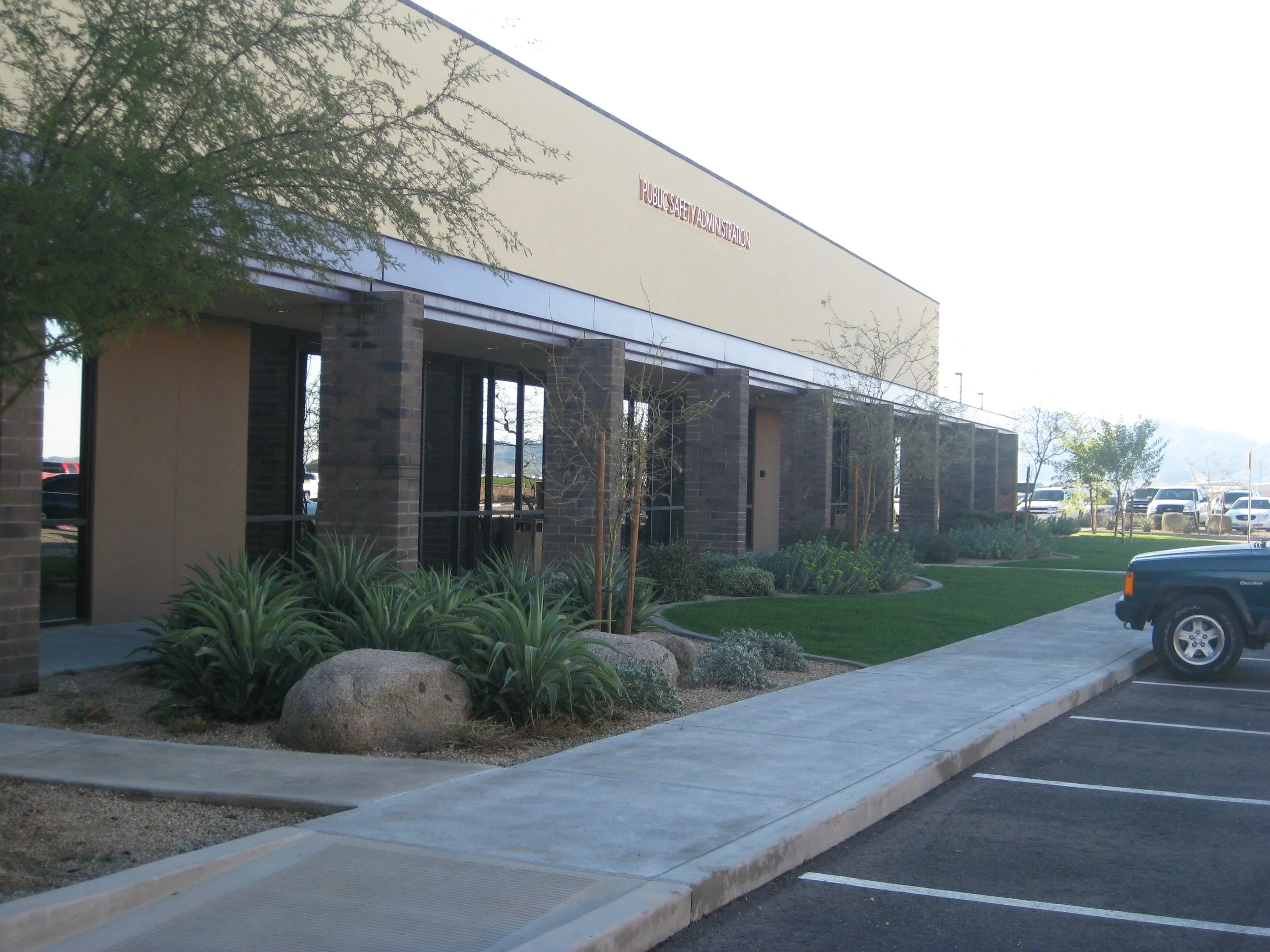 Commercial office building with desert landscaping and parked vehicles.