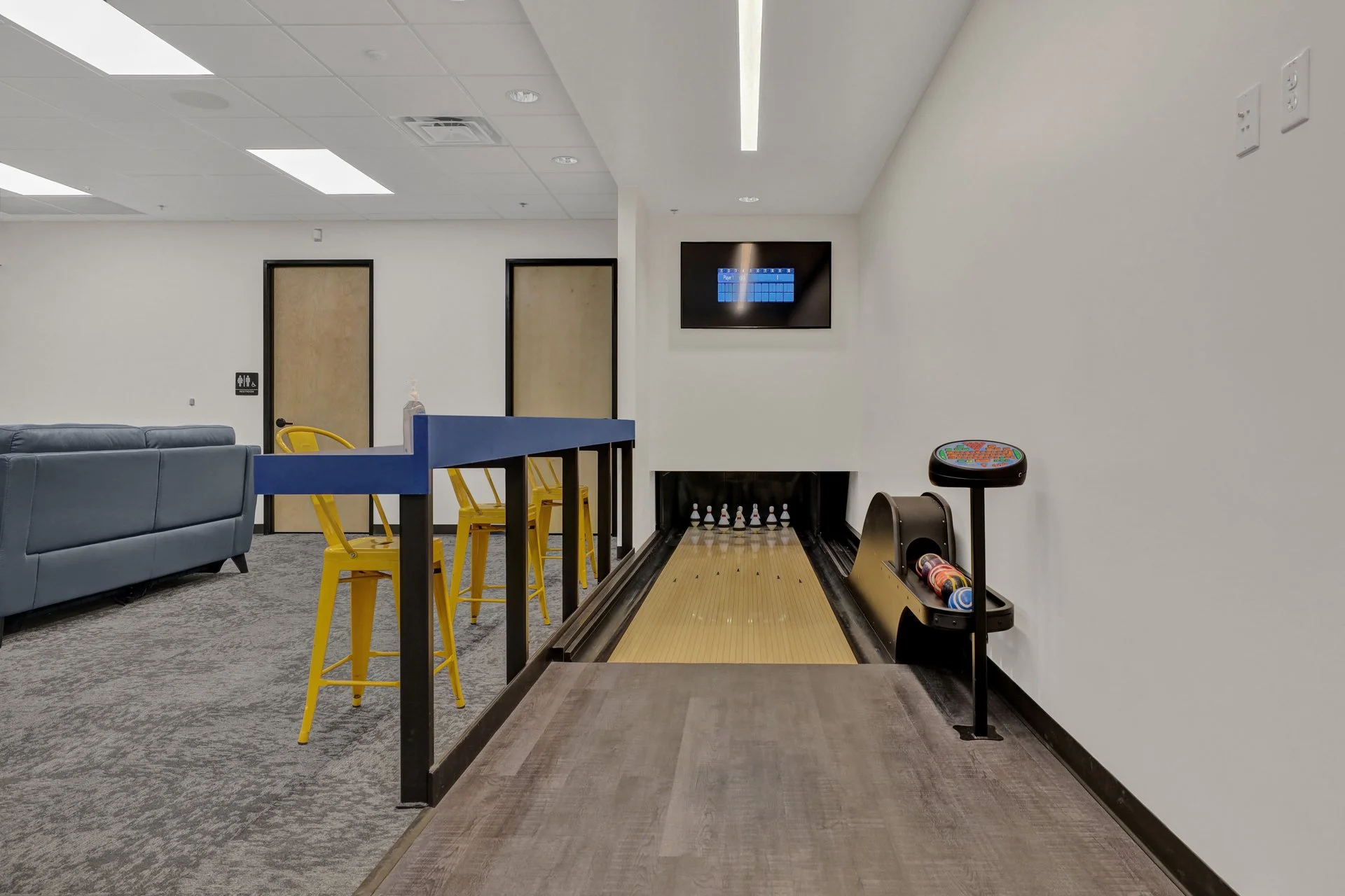 Contemporary indoor mini-bowling lane with yellow chairs, blue partition, and modern decor.