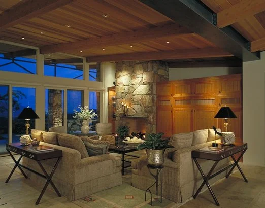 Cozy living room with stone fireplace, beige sofas, wooden ceiling, large windows, and decorative elements.