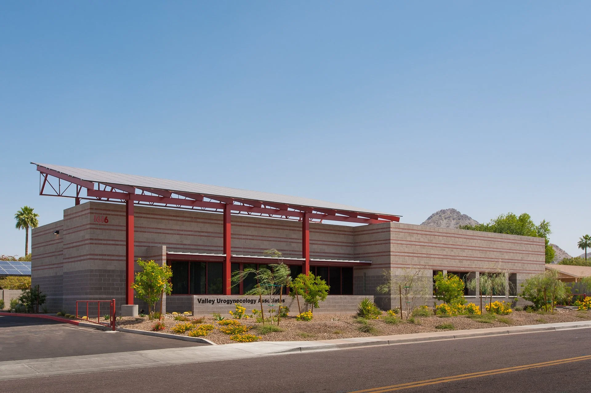 Modern medical office building with solar canopy, desert landscaping, and clear blue sky in an urban setting.