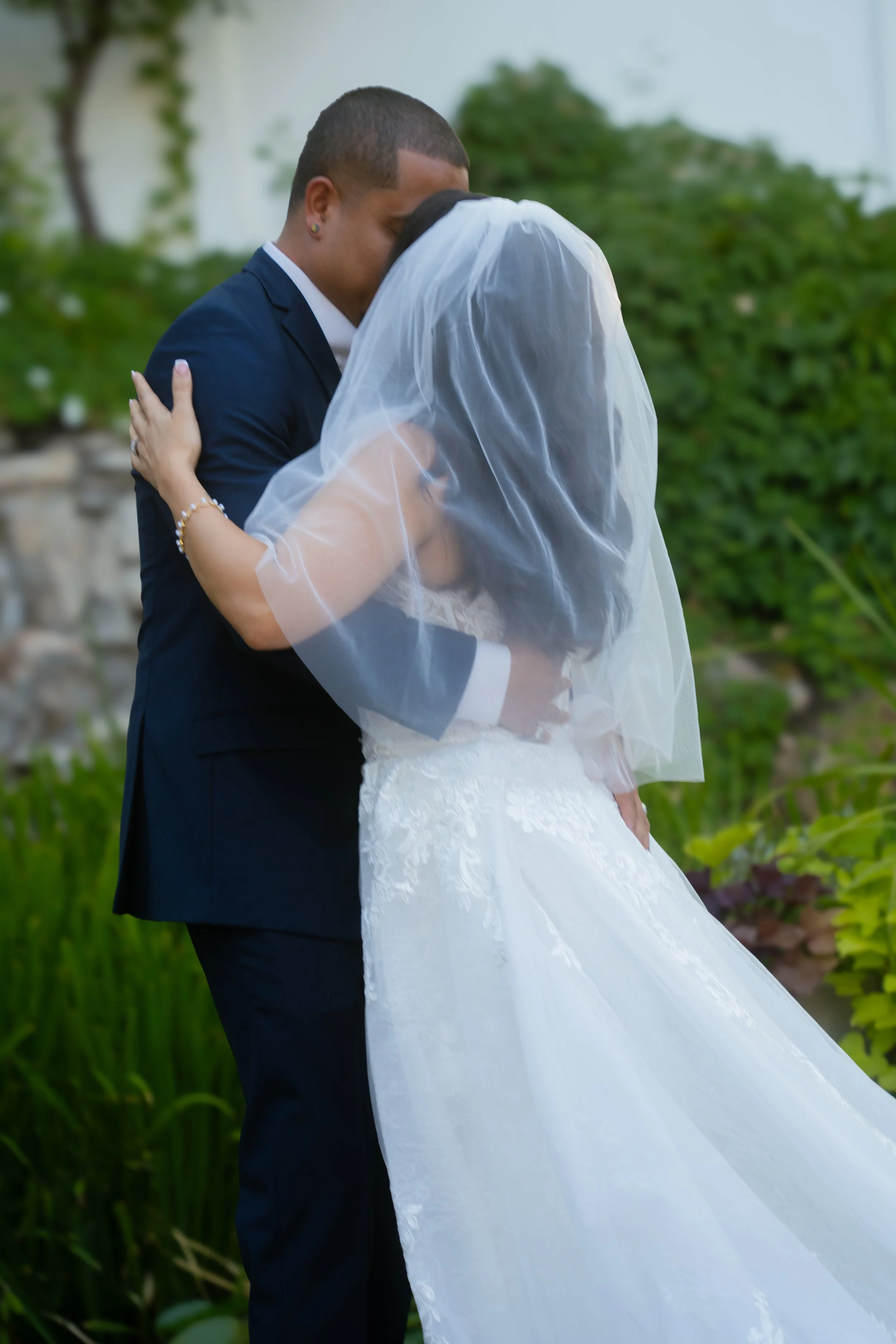 A bride and groom sharing a kiss outdoors, with greenery in the background.
