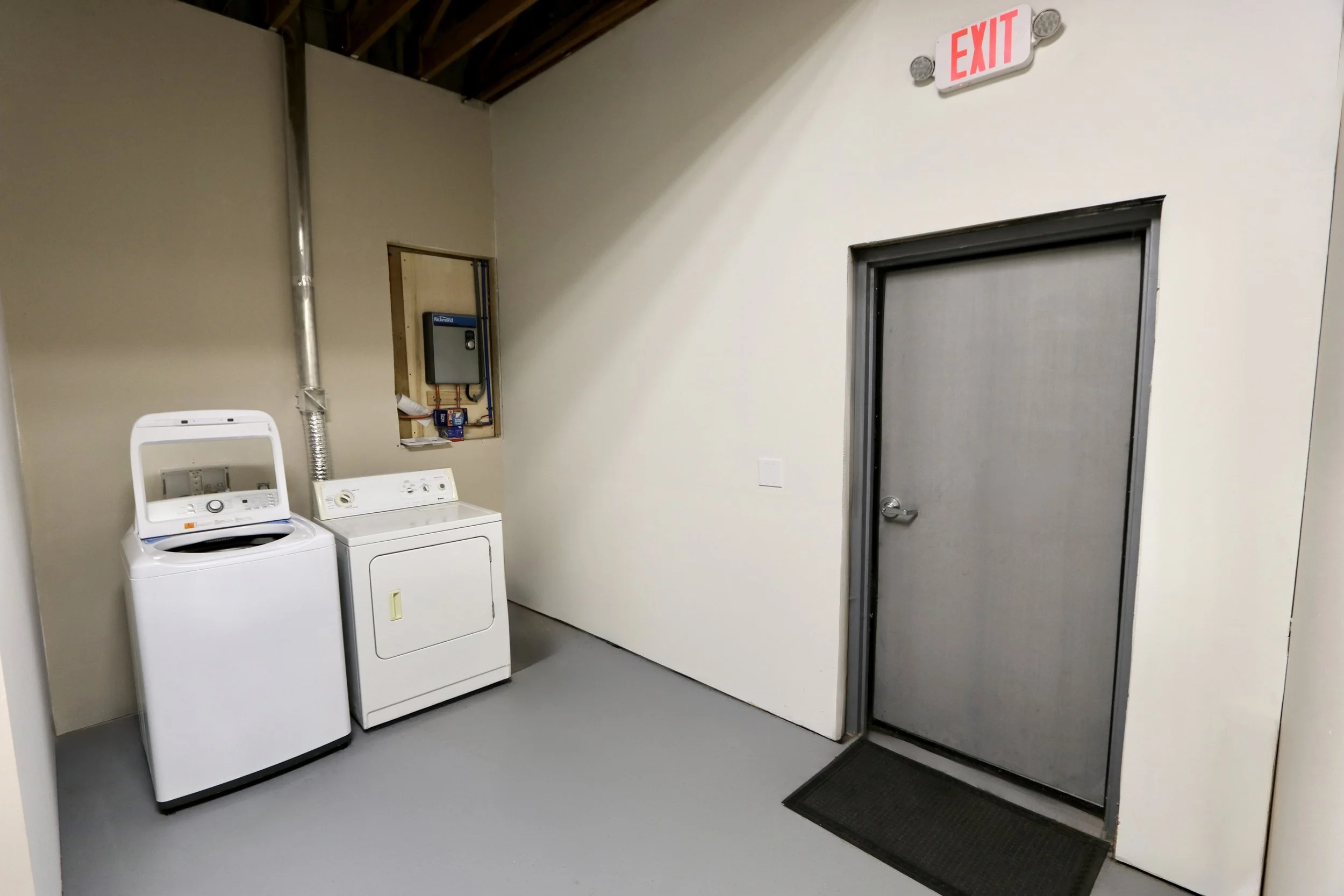 Laundry room with a washing machine, a dryer, a utility panel, a door with a screen, and an exit sign above the door.