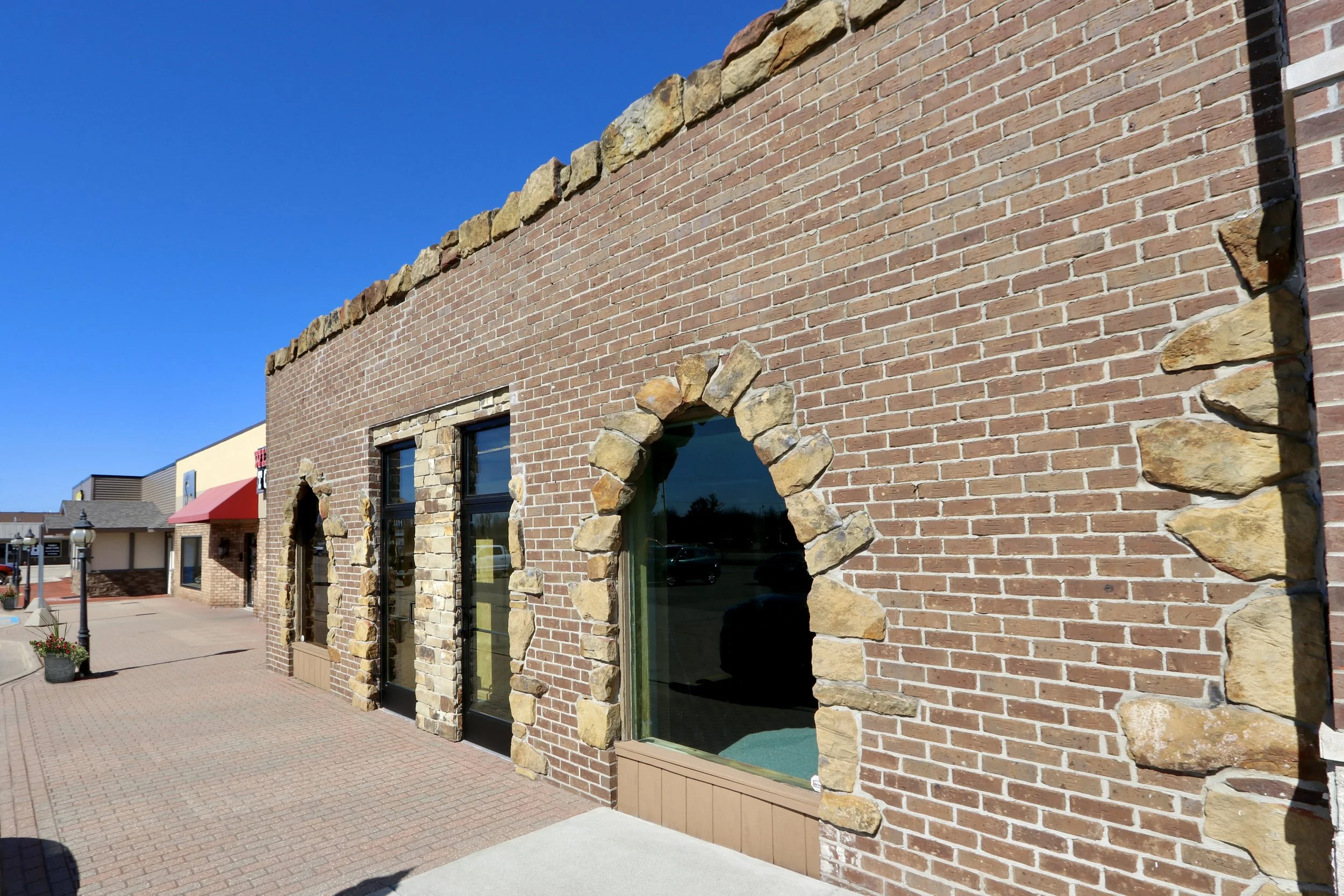 Brick building with stone accents around windows and top, sidewalk in front, clear blue sky.