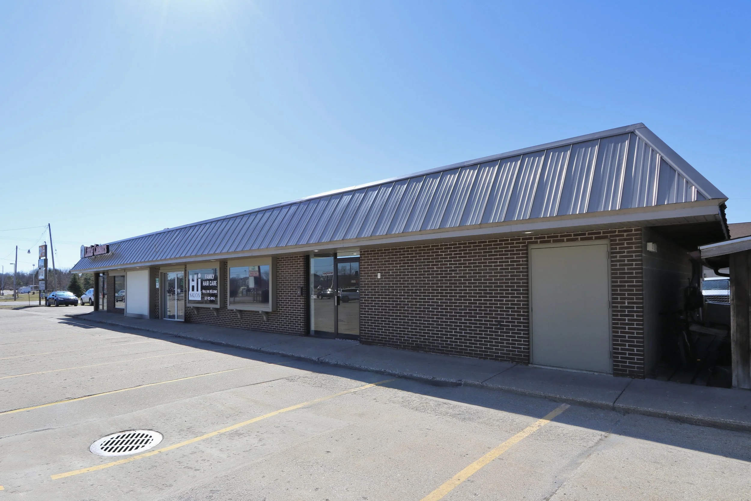 Exterior of a brick commercial building with a metal roof, parking spaces, and clear blue sky.