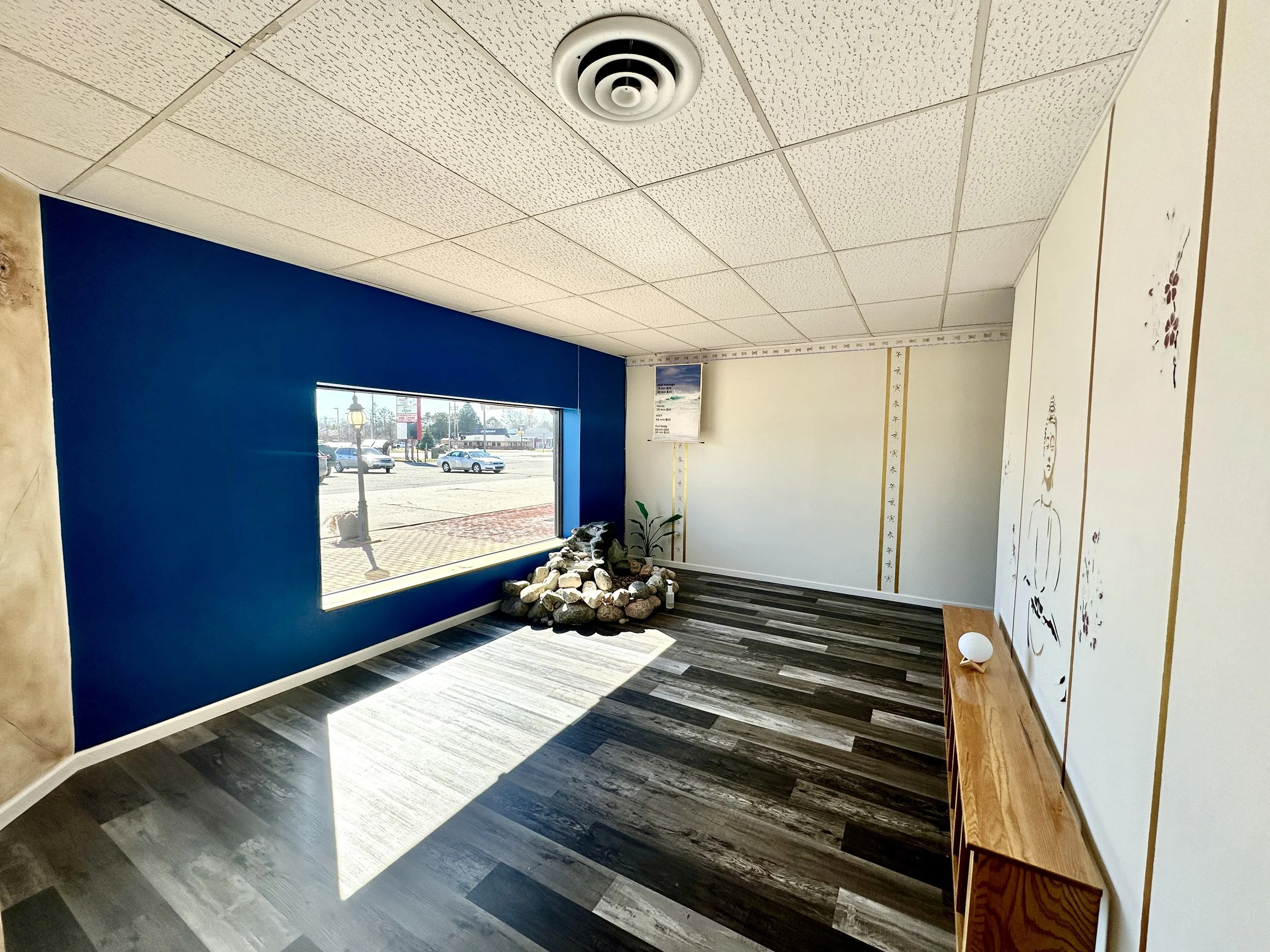 Empty room with a large window, blue accent wall, decorative rock arrangement, and a wooden shelf with a white spherical object.