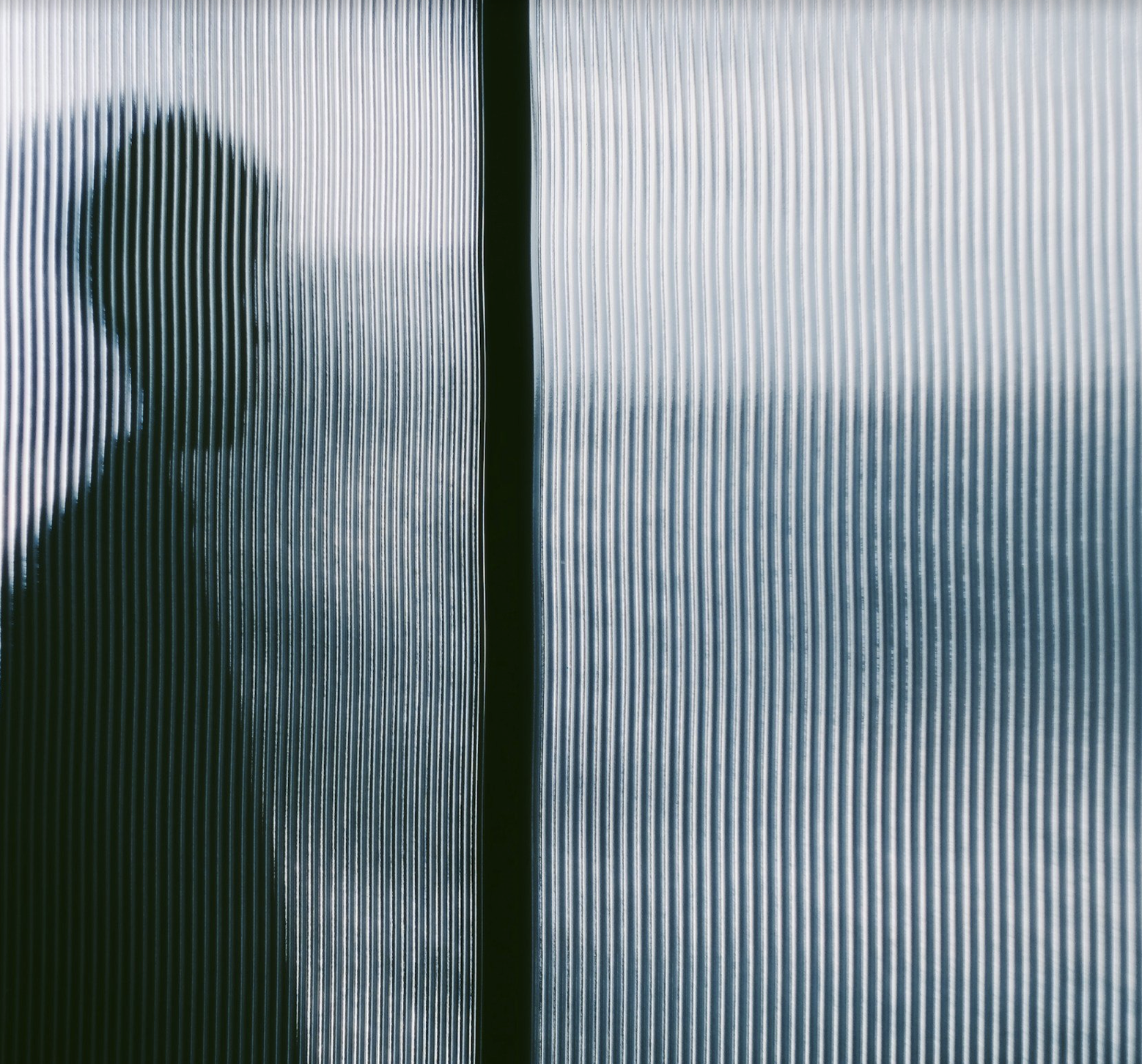 Silhouette of a person's head and shoulders seen through a frosted glass wall with vertical ridges.