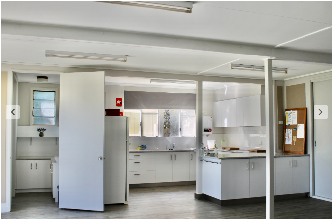 Empty kitchen with white cabinets, countertops, and a bulletin board on the wall.
