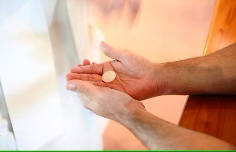 Hands holding a round white pill over a wooden surface with a blurred background.