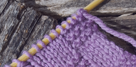 Close-up of a knitting project with purple yarn on wooden knitting needles.