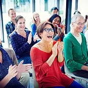 Group of diverse people laughing and clapping at a live event or presentation in a bright room.