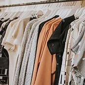 Clothes hanging on a rack, including sweaters, jackets, and shirts in various colors and patterns.