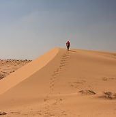 Person walking on sand dunes in a desert landscape.