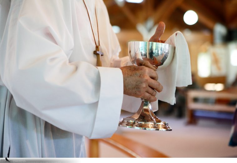 Person dressed in white robes holding a silver chalice during a religious ceremony.