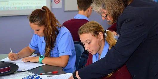 Teacher assisting students in a classroom setting with writing activities.