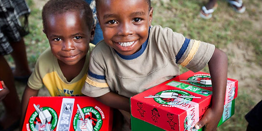 Two smiling children, one holding a Christmas-themed gift box
