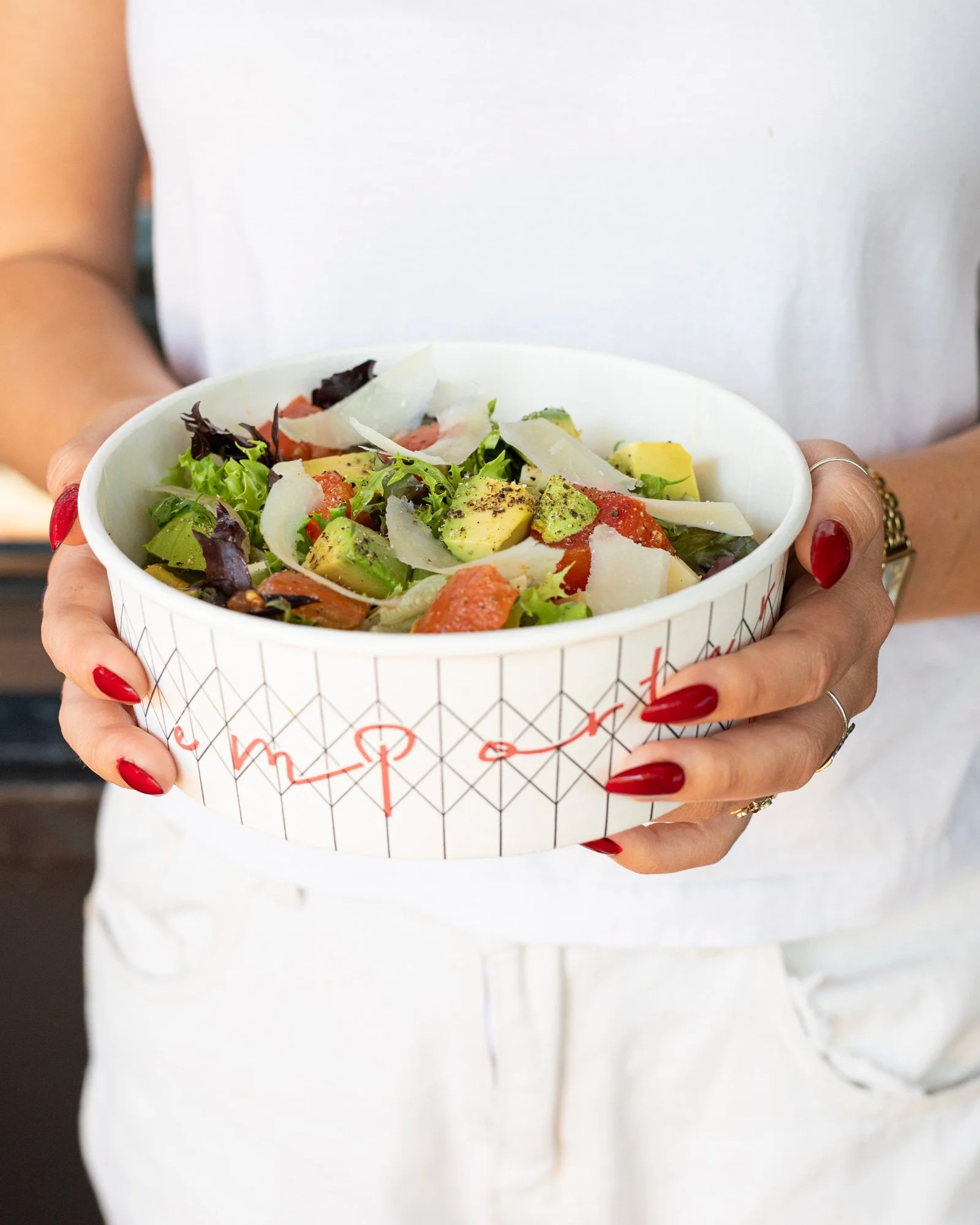 Photo of woman holding mixed lettuces, tomato & avocado salad to-go at zinqué, a French restaurant