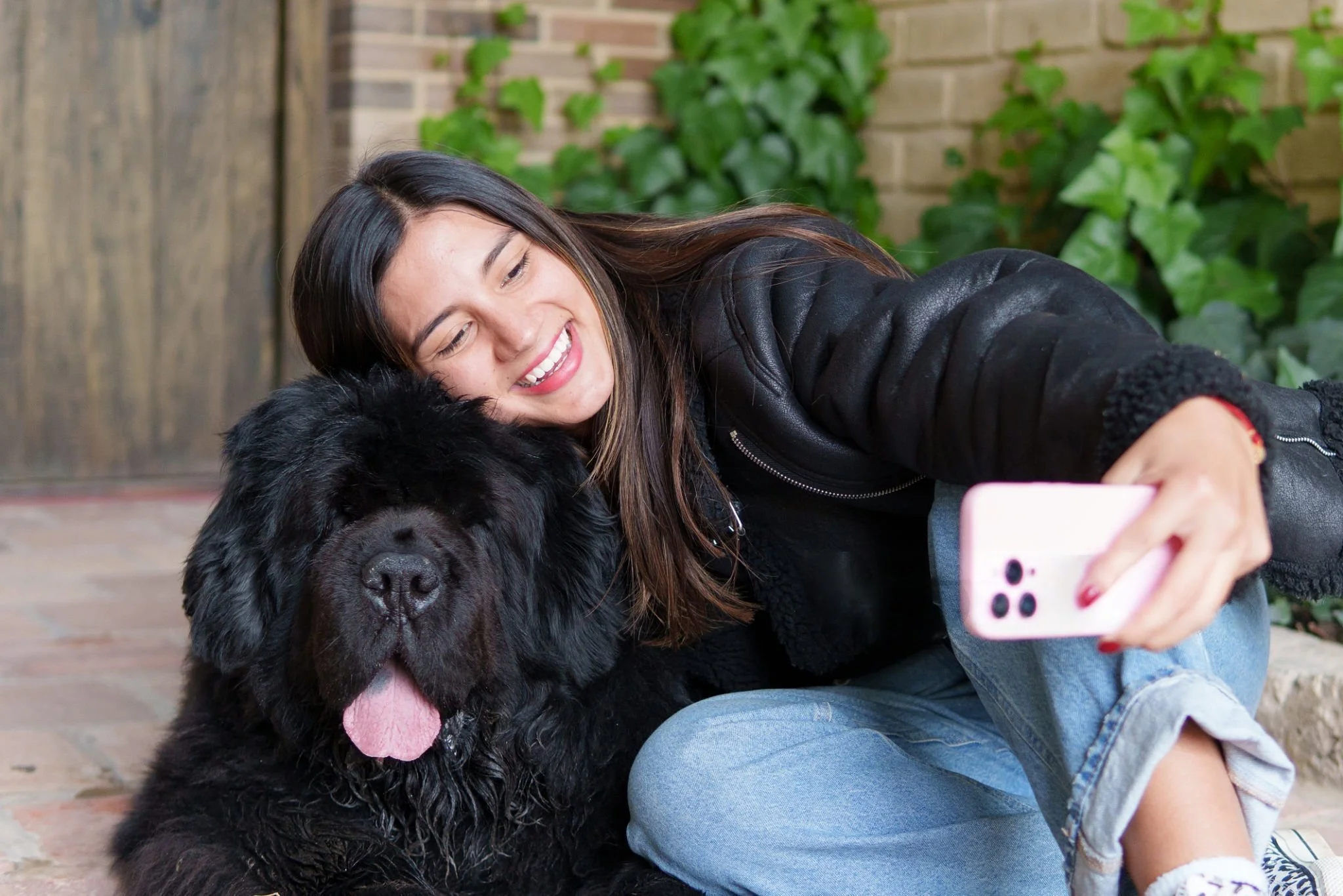 Young woman smiling and taking a selfie with a large fluffy black dog outside