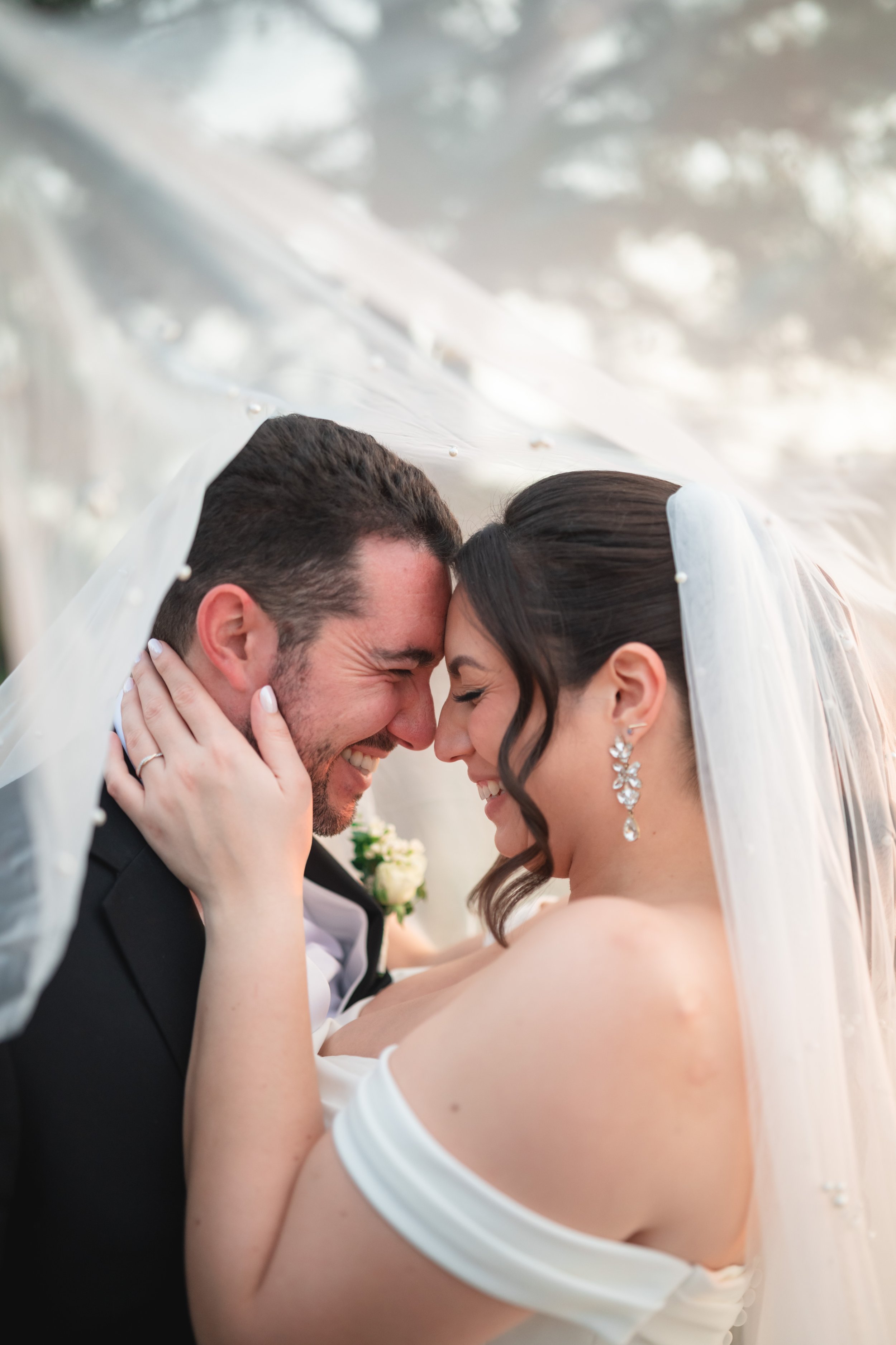 a couple is looking into each other smiling while underneath a veil