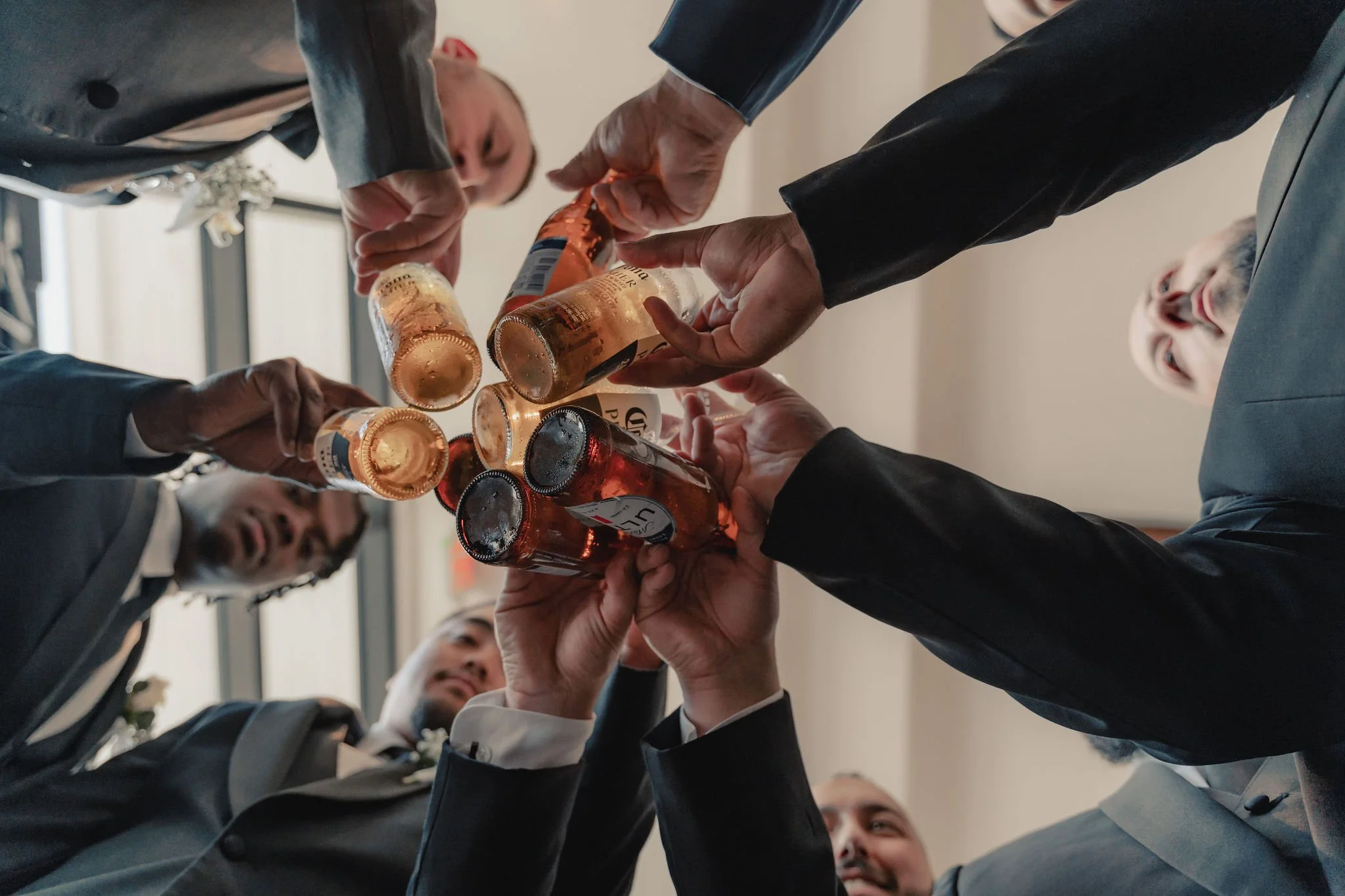 Group of people in suits raising bottles of beer in a toast at a celebration or gathering.