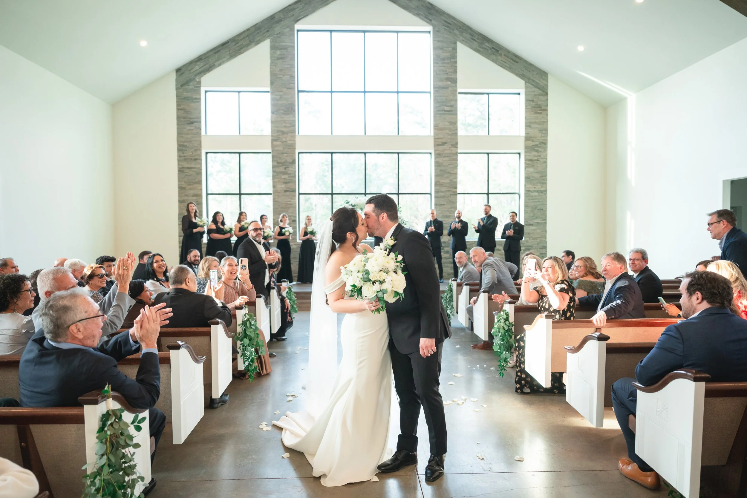 a bride and groom stopping in the middle of the aisle to kiss for the camera