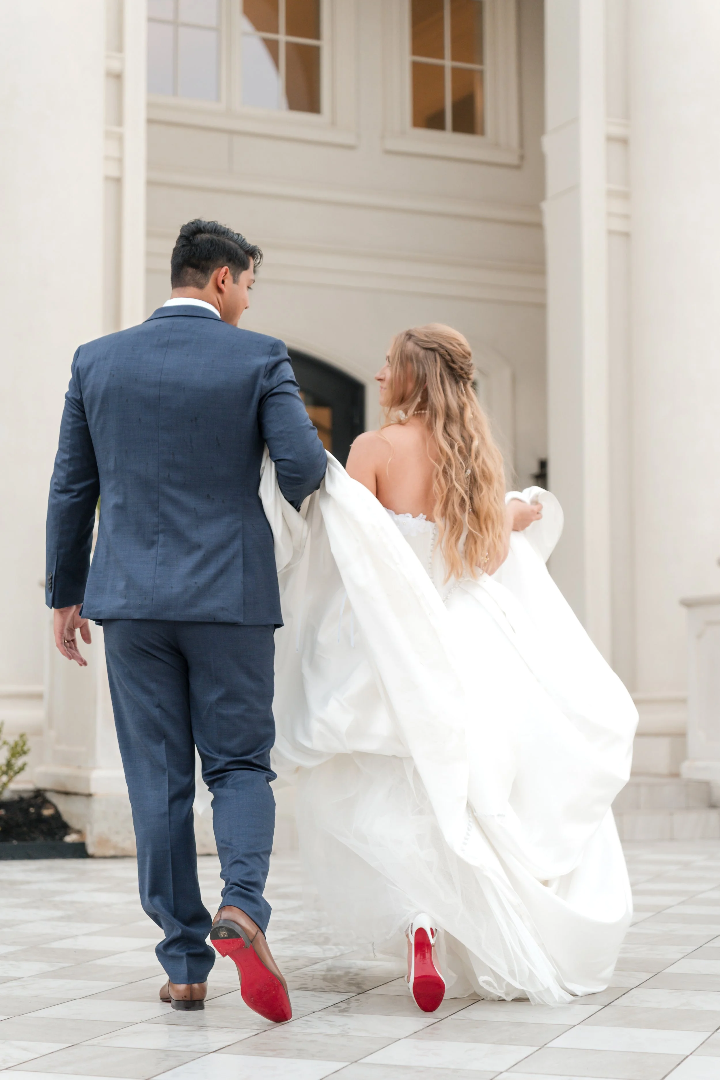 a girl is walking with a man holding her dress  and wearing red bottoms