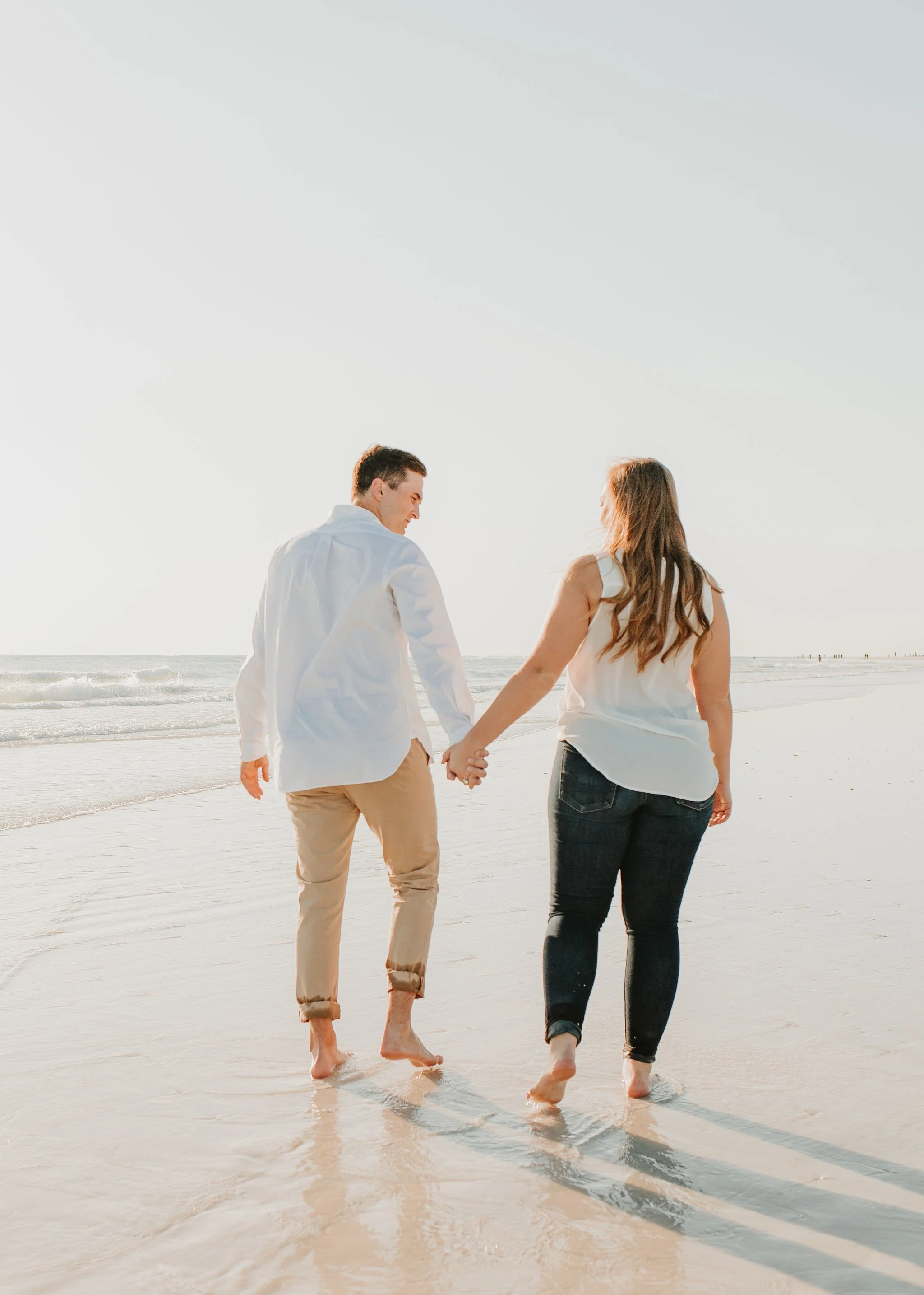 A couple walking hand in hand along the beach at sunset.