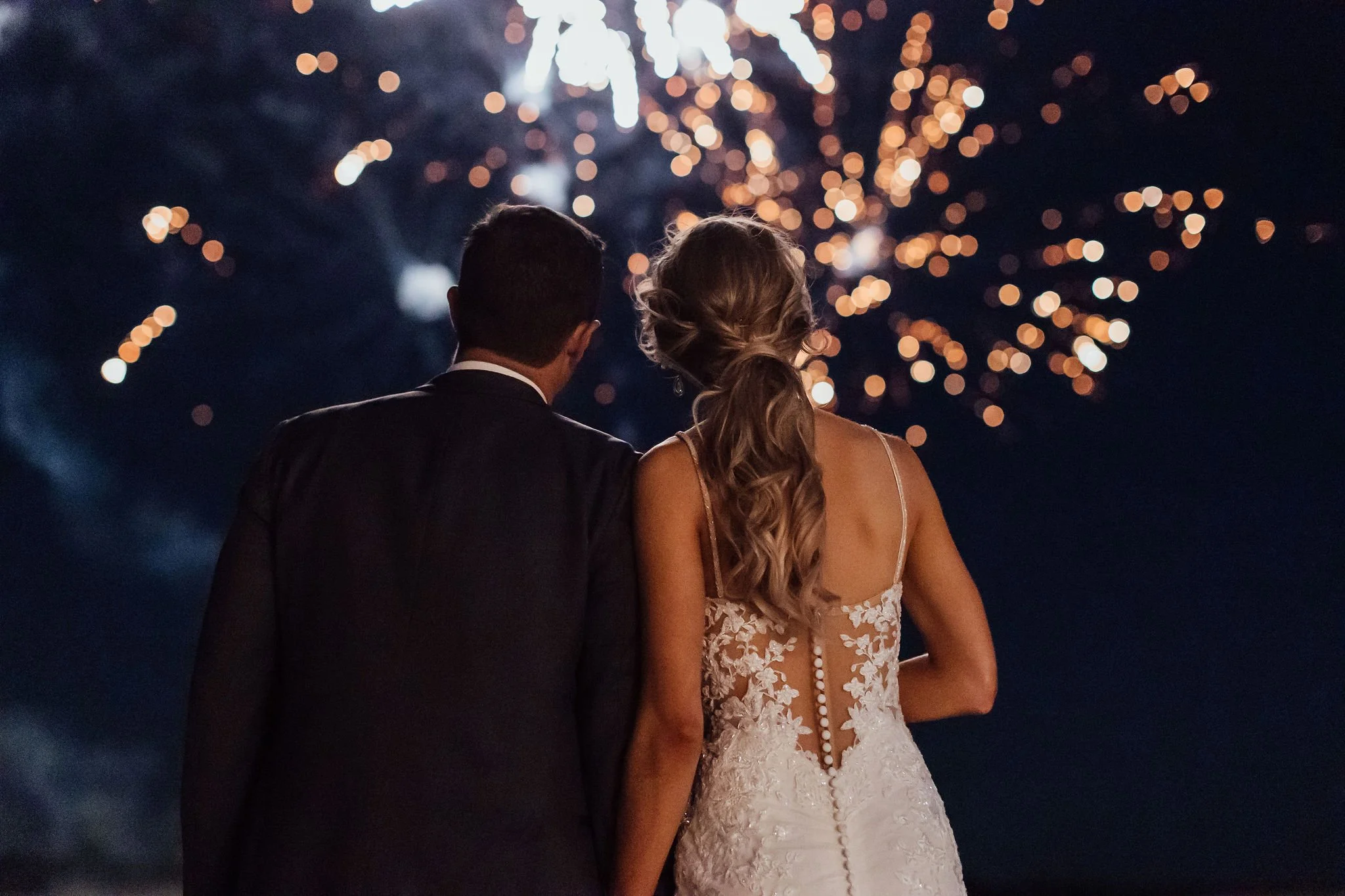 A bride and groom watching fireworks at night.